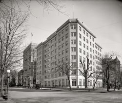 Washington, D.C., circa 1917. "U.S. Department of Justice, exterior, Vermont and K streets N.W." Harris &amp; Ewing Collection glass negative. View full size.
I have to say...I like Vermont Avenue better in 1917 than the way it is today. Looking at Google Street View, the DOJ building is still there, but improved into something ugly, and the lovely old buildings behind it are gone, replaced by sterile blah. Oh, 1917, where are you?!
Buildings and View CamerasFirst, I have to say I just discovered Shorpy's and it's absolutely marvelous! I could - and will - spend days looking through it.
In the Department of Justice shot, the odd skewing of the windows would indicate that the photographer has used the tilting front of the view camera to make sure the external edges of the buildings are vertical, which they are.  Not all lenses had enough coverage to allow you to do this to any great extent, and the result was a darkening of the upper corners ("vignetting"), which has happened here.  For the next 92 years, photographers often darkened the upper corners during printing.  Sometimes it did a nice job of framing a print, but it's interesting to speculate how often they were imitating the older shots.
The same thing happened in landscapes - the slow glass plates meant slow shutter speeds, which turned waterfalls and rapids into a misty vapor.  To this day landscape photographers duplicate that effect, even though it doesn't look anything like moving water.
DOJ Building HistoryThis was the long-waited for replacement of the temporary offices located half a block away at 1435 K street.  Congress first authorized construction of new offices for the Department of Justice in 1889. After sixteen years of inaction on this project it was eventually built amazingly quickly once a site was finally chosen.
The Federal Housing Administration took occupancy in 1934. Sold in 1953 to GEICO, the Government Employees Insurance Co. moved in in 1956.  GEICO moved out in 1967. Not sure when the structure was razed/refaced to make way for current building



Washington Post, Dec 17, 1916 


Built In Record Time
New Home Ready for Department of Justice January 1.

Receiving the finishing touches now, the Department of Justice building, at the corner of Fifteenth and Vermont avenue, will be ready to turn over to its future occupants before January 1, having been completed in the record time of five months from the pouring of the first concrete.
It is eight stories in height, each story being laid out for the convenience of one of the six divisions of the department, with one floor for the Attorney General, and his immediate staff, and another for the very extensive department library.
It is built entirely of reinforced concrete, with two-story facade of limestone, and the balance faced with hytex brick trimmed with stone.  The floors are steel beams and concrete, the whole completely fireproof.  It is equipped with smokeless boilers, [central] vacuum cleaners, and running refrigerated water, and is finished in mahogany throughout.  Three elevators give service from basement to roof.
The building was started July 27 under penalty of $500 a day for overtime in delivery after January 1, has been pushed to completion under the personal supervision of Harry Wardman, who at times has had over 600 men at work on day and night shifts.
Great difficulties had to be overcome in obtaining the necessary material, owing to the existing car shortage and the demands made upon the steel companies by munitions manufacturers and for railroad and structural material by warring nations of Europe. The investment is reported at approximately $600,000, and the lease to the government is at $26,000 per year for five years from July 1, 1917.

View Larger Map
Some architectgot paid good money to turn those clean, classic lines into a monstrosity.
(The Gallery, D.C., Harris + Ewing)