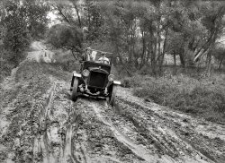 1920. "Duplex truck, Culpeper trip." Nat'l Photo glass negative. View full size.
BannerCan anybody make out what the banner in the bed of the truck says?
["Washington D.C. -- 'On Time All the Time' -- Baltimore Md." - Dave]

If you don&#039;t like the way I drive...Then get out and walk!
Wait right there, ladiesIs he testing the road first and then going back for the girls?
Stick-in-the-muds"Yeah, right, we'll go with you and get stuck in the mud" ... is what I can picture the smart young ladies in the background saying.
What the heck!Does anyone know what those two rectangular panel-like things are which are strapped to the front axle and are dragging in the mud? I know a few things about vehicles of this period but I have never seen anything like it.
[Where I come from we called them "license plates." - Dave]

So they are!At full size view I was not detecting that they had numbers on them; in your attached blowup I am willing to own that they are license plates indeed - even where I come from! Can't get away with hanging my plates underneath on my front axel axle in Virginia today (I despise having to mount front plates on my 1930 Model A 5-window coupe!)
Pavement good!As I was navigating my way over icy pavement this morning, I was cursing it and thinking that back before roads were paved, it was a lot easier to walk on it during the frigid winter months. But this photo has reminded me that pavement is a very good thing indeed!
To A or not to ANo A ever had a radiator shell like that, and there is no way that truck is 4 wheel drive. Take a look at the front axle... Duplex is the brand, but maybe they were responsible for the 4wd conversions for As. If the date is correct, the picture predates the A by about 8 years too!
[On the radiator it says "The Duplex Limited." Below, a 1922 ad. - Dave]

Duplex Model AThis appears to be a Duplex Model A - powered by a 4 cylinder engine generating an impressive 25.6 horsepower (hold on tight!)
If you have a heavy hauling problem and do not already know the Duplex 4-Wheel-Drive, talk to the Duplex dealer and let him give you the facts at first hand.
The Duplex Truck Company is the Originator of the 4-Wheel Drive principle and today its most successful exponent.
There is pull and power in every wheel — and the Duplex 4-Wheel drive keeps going under conditions that are simply impossible for any rear wheel drive trucks.
The Duplex 4-Wheel drive is setting new records of truck efficiency for lumber and Logging Company; Road Builders; Oil Companies; Coal Companies Mining Companies; Grocery Companies; Trucking Contractors—in fact in all lines where there are heavy loads to be hauled.
The point is the Duplex 4-Wheel Drive is daily proving to a very economical truck for hundreds of owners who used to say it was too big for their needs.

A couple of Google Book links:

1922 Official Handbook of Automobiles
(page forward to see other models)
Motor West (1920 advertisement)

Duplex banner mysteryCan you turn the truck by 90 degrees please Dave?
I think I see a banner with "DUPLEX" in in the middle of it.
[There's a photo of the banner in the third comment from the bottom. - Dave]
(The Gallery, Cars, Trucks, Buses, Natl Photo)