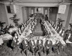 Washington, D.C., circa 1920. "Civitan Club." Caught in the middle of the soup course. Harris &amp; Ewing Collection glass negative. View full size.
Carrot soup?So few of these gents are bespectacled that I am wondering if the carrot soup truly aids the eyesight. I can't imagine a group of this style today with such a minimum of visual aids.
ClassyThe two guys up front wearing spats.
So formalThe spats are spiffy!
Back SeatThe two guys without black or white tie seem to be relegated to a separate side table.  I guess they just didn't know how to dress for the occasion.
!!!Ring Ring!!!Wonder if the phone jangled during the proceedings?  It wouldn't go to voicemail, that's for sure.
DifficultI can't find anyone in the picture that seems pleased to be there.  But I do like the design of those chairs.
Duck!Reminds me of the Louisville Slugger scene from one of the mafia movies. I believe it was 'Capone' or the like.
CaponesqueI love a man in spats!
And at the kiddies&#039; tableMaybe they were banished there for showing up out of tux. After all, there ARE two empties inside the horseshoe next to the head table. Presumably those two no-shows were powerful enough to warrant choice seating and our two lads were not. At least they weren't told, "No soup for you."
So which is it?Is this a white-tie affair or black-tie?  Apparently the invitations weren't specific and assumptions were made.  Thank goodness the gents in front remembered their spats.
And what's up with the two guys off to side?  They look quite a bit younger and they are not in Evening Dress - maybe that is the Civitan Children's table. 
Farewell dinnerThe massive floral arrangement at the back of the room would have me peering over my soup plate wondering if a casket was hidden in there.
Civitan Club Luncheon Minutes

Washington Post, Feb 24, 1922

The Civitan club held its weekly luncheon at the City club yesterday.  E. Barrett Prettyman won the attendance prize.  Ernest Greenwood announced that a hat will be given the member who produces the best slogan for the club.  Robert Armstrong, president of the National Press club, was speaker.




Washington Post, Mar 10, 1922

Better and cheaper automobiles and clothes are now on the market, Chester Warrington, automobile dealer and H.S. Omohundro, tailor, yesterday told the Civitan club at its weekly luncheon at the City club. Three-minute talks by members featured the meeting.
I.L. Goldheim, haberdasher, said that once again men are getting quality clothes.  Ira La Motte, manager of the Shubert-Belasco theater, told the club that Washington was the only bright spot in a disastrous season for theaters throughout the country.  Oliver Hoyem, connected with the publicity department of the American Federation of Labor, and Dr. Grant S. Barnhart, physician, also spoke.




Washington Post, Mar 13, 1922

The Civitan club is strongly opposed to the recent action of the board of education authorizing the use of branch libraries in the public schools by white and colored children indiscriminately, President Rudolph Jose announced yesterday.
Resolutions adopted by the board of directors of the club describe the action of the school board as "vicious" and detrimental to the interests of both white and colored.




Washington Post, May 19, 1922

Work has been started on the new additions to the Civitan camp, it was announced yesterday at the weekly luncheon of the Civitans at the City club. It will be decided during the present week the exact time that the camp will open to receive poor children of Washington.
Dr. S.M. Johnson delivered a short talk on the necessity of completing the Lee highway, citing the great help and money the road would bring to business men of this city.




Washington Post, Sep 8, 1922

Future plans for the "Ladies' night" entertainment, on October 12, were discussed at the luncheon of the Civitan Club in the City Club yesterday, Charles Crane is chairman of the committee on arrangements. It was decided to visit the Baltimore Civitan Club on September 22, at which time a special golf match between the local club and Baltimore will be held. Chester Warrington is captain of the Washington club team. A report of the camp, which closed last Saturday, was read and approved.  Rudolph Jose presided. 
The club will meet Thursday night in the City Club, instead of in the middle of the day.




Washington Post, Oct 27, 1922

Stricter observance of the regulation regarding the signals to be made by motorists at the street intersections was urged by C.J. James at the luncheon of the Civitan club yesterday at the City club.  Mr. James asserted that many drivers merely drop their arms on the outside of the car, no matter what they intend to do.  This sort of signal, he said, means nothing, emphasizing definite signals required by law should be used. 
C.H. Warrington declared that pedestrians should be regulated as well as motorists. He declared also that the proposed reduction of the automobile speed limit to twelve miles an hour would cause great congestion in the business district.




Washington Post, Dec 26 1922

The Civitan club will hold a luncheon meeting at 12:30 today at the Lafayette.

The ShiningWhere are Lloyd and the caretaker?
Japanese LanternWhat are those suspended boxes?
Civitan ClubsMy father, Fred T. Massie, was very active in the Civitan Club of Dallas. They were a civic group, which meant they did things for the good of the city. Such as provide for orphans to go to camp. They met once a month at the Adolphus Hotel. Most of the powerful men in Dallas were members of "The Civitan." It was a way to give back to Dallas. 
My mother, Mary Massie, was involved in "The Ladies of Civitan." I remember going to the Christmas meeting with her. We had lunch and then put Christmas stockings together for needy children.
I don't know where this picture was taken, but there were Civitan Clubs in cities all over the nation.
[As noted in the very first word of the caption, this was taken in Washington. - Dave]
Young clubAccording to Wikipedia, Civitan was organized by a group of men in Birmingham, Alabama in 1917. These men broke off from a local Rotary club, because of differences they had with the direction they perceived it was going. Civitan is very active today and still headquartered in Birmingham.
FormalwearIt's amazing how little the style of tuxedos has changed in the past 90 years. 
Oh, sorry, wrong banquetIt was too late for apologies. Machine Gun McGurk and his Thompson had spoken.
Japanese lanternsThey are light fixtures -- thin brass or some other gold-coloured metal frames with lacquered paper or parchment fillers and painted designs.
Black tie vs. White tieWhat this picture shows is the gradual replacement of traditional white tie formal dress by black tie.  At this point in history, the invitation would probably have simple said formal, or, I suspect, it would not have made the designation at all.  The attendees at a function like this would have automatically known what to wear.  Events like this would have seen a mix of white tie, with a sprinkling of black tie.  The tuxedo, as we know it, was first worn around 1890, as a more casual form of formal dress for men (I know, an oxymoron.) At this time the dinner jacket would be worn with a black waistcoat.  Later on the cummerbund became more popular.
A few more interesting details here:  there is one man with a white tie and a black vest.  This would have been much more common in the late 19th century, but was definitely passe, but not proscribed, by 1920. The variety of collars and ties among the black tie wearers is also interesting.  With white tie you only wear a stand up collar and white bow tie.
The black dinner jacket (aka tuxedo) admits a greater range of acceptable collars and ties.  Two gents in the front have interesting lay down collars with some sort of criss cross tie that doesn't look like a standard bow tie.
And of course everyone knows that an outfit like this is NEVER worn before 6.  Before 6 (really up until 4) a gentleman would wear a cutaway coat (tailcoat with tails that curve away in front, as opposed to the sharp right angle of the white tie tailcoat), with striped trousers, a gray vest and a cravat.
BTW, I DON'T think those are spats.  I think those shoes have patent leather on the lower part and calfskin on the upper part.  But I'm not sure.  True spats would show a strap under the sole of the shoe.
(The Gallery, D.C., Harris + Ewing)