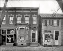Washington, D.C., circa 1927. "Al Jolson's parents' house," 4½ Street S.W. Harris &amp; Ewing Collection glass negative, 8 x 10 inches. View full size.
Narrow passageSmall, but scary, alley.
Paging Big Joe TurnerI wonder if Big Joe Turner (who would've been 16 at the time) might have seen a poster for that show?
The Boswell Sisters also had a song called Rock &amp; Roll out around this time, must've been something in the air...
Dearest Spot on EarthNote that address is in the southwest quadrant. I don't think there was a 4½ Street in the northwest.



Washington Post, Jun 24, 1923 


Native Washingtonians Succeed in
Varied Fields of Endeavor

...
To the southwest section of Washington as well as America generally the stage is typified by one name, "Al Jolson," for he is the pride of that neighborhood where he lived from the time he was a child of eight after coming to America from Europe until the dawn of fame drew his steps away from the Capital.
Down in the substantial home at 713 Four-and-one-half street southwest, his boyhood home and where his father, the Rev. M.R. Yoelson still resides, there is always joy when "Al" is coming to town.  For they know that although he is a personal friend of President Harding, who always tries to see his show and appreciates his humor and genius to the full, the "dearest spot on earth to him is Home, Sweet Home" and his big car caries him swiftly away from the uptown theater to his home where a reunion with his dear ones awaits him.
The boys and girls at Jefferson school, just around the corner, treasure every scrap they can learn of Al Jolson, for he is one of their own, "a Jefferson school boy" through all his healthy, happy boyhood, a marble champion, a baseball player and popular among his mates.
...

A million milesSo this is where he would walk a million miles for one of her smiles?
also don't know what the shake, rattle and roll refers to on the signs but for sure it isn't very early rock and roll.
Brrrrr....Is the coat lying on the bench possibly the cameraman's or did someone just walk away from a nice coat?  Also it looks like the woman in the picture is getting ready for a shave!
The 3 crosses in the architecture above "713"....were these common for that day?
[Those are fleurs-de-lis. - Dave]
Woman and screenI love the barely-visible cross-armed woman in the barber shop. She looks so unamused! Also, what's the deal with the screen over the barber's door? It looks like it could be pulled down to cover the whole doorway.
[The lady might be cardboard. - Dave]
Kiatta vs. TaylorFlyer in Sam's window....



Washington Post, Mar 25, 1927 


Kiatta vs. Taylor on Mat

George Kiatta, Syrian mat expert will meet George Taylor in a wrestling bout at the Mutual theater tonight.  Taylor has recently won victories over Dutch Green and other good middle-weight wrestlers.

ThrilledI am absolutely thrilled to find these photos.  I am a Jolson fanatic from way back.  I am going to share these photos with a friend of mine who is also a Jolson addict.
Fixer upperI would have thought that with all his money that Al would have gotten the brick pointing repaired under those first floor windows. Or maybe his father refused the offer to do some repairs because Al's money came from the stage...or have I just watched "The Jazz Singer" too many times?
DetailsAnother example of stone lintels, neatly done. Al Jolson's brother was the father of a buddy of mine at college. An interesting family!
Shake, rattle etc.Couldn't find much info on the Jones boys.  Did find an old Eddie Cantor reference to Archie being listed as a trombone player on a record from early 1920s.  Maybe they were the first to shake rattle and roll.
ContrastesOstentosa barandilla de fundición junto al callejón de mala muerte...
Flores de Lis (?), en todo caso, invertidas. Dave)
Heavy TypecastThe guy in the second-hand store looks like he could be typecast as the heavy in any of the period films.
I remember seeing......"The Jolson Story" and "Jolson Sings Again" when I was  kid. Larry Parks played Jolson. If I recall correctly, they liked to play them on New years Eve. I enjoyed them as kid, but I'll bet they wouldn't play very well today...all that blackface stuff, you know.
Four and a HalfJustice Douglas had his opinion of the SW neighborhood and today, 55 years later, I have mine.  The redevelopment that took place there may offer residents more plumbing, electricity and other conveniences, but all of the texture, history, aesthetics and character have been destroyed. Today, the neighborhood has all the bland "character" of similar mid- to late-20th century "developments."
Every trace of the old place is gone, even the undeniably charming street name of 4½. That part of history will never come back in this neo-wasteland.
I'd take Italianate cornices, scary alleys and quirky ironwork any day over the sterile blandness of a fake suburban utopian fantasy.
The deal with the screen...The screen is not meant to be pulled down. Rather, it was placed there to fill the void above a screen door (no longer present in the photo). If you look closely, you will see that the door to the barber shop is slightly taller than the average door. The right side of the jamb (below the weird screen) has been supplemented with a vertical board upon which are mounted two hinge halves.  It is upon these that the erstwhile screen door (of a more conventional height) hung.
A less-charitable view of that blockThis spot is close to the site of the department store at 712 Fourth Street, S.W. where the landmark U.S. Supreme Court case of Berman v. Parker arose. According to Justice Douglas's 1954 opinion for the Court, "Surveys revealed that in Area B, 64.3% of the dwellings were beyond repair, 18.4% needed major repairs, only 17.3% were satisfactory; 57.8% of the dwellings had outside toilets, 60.3% had no baths, 29.3% lacked electricity, 82.2% had no wash basins or laundry tubs, 83.8% lacked central heating. . . . The entire area needed redesigning so that a balanced, integrated plan could be developed for the region, including not only new homes but also schools, churches, parks, streets, and shopping centers. In this way it was hoped that the cycle of decay of the area could be controlled and the birth of future slums prevented." 
Shake, Rattle, and Roll, 1919Shake, Rattle, and Roll (Who's Got Me) was recorded by Al Bernard in 1919.  Have a   listen! It's about gambling with dice.  My guess is the event the poster advertises is along those same lines.
History of 4½ Street SW"During the late 19th century (when today's 4th Street was named 4½ Street in Southwest), these streets were lined with small shops and were centers of a Jewish immigrant community. A synagogue of the Talmud Torah Congregation opened in 1906 under the direction of Rabbi Moses Yoelson. One of his sons was singing star Al Jolson."
"Then called 4½ Street, by 1900 this street was a dividing line between white residents on the east and blacks on the west. When renamed 4th Street between the world wars, both groups joined together and persuaded the city to widen and repair the street, add modern paving, and improve lighting. Community activist Harry Wender reported that the neighborhood commemorated its victory by holding the "biggest celebration in the history of the city" and that "it was the first time that Negroes and whites paraded together in the history of Washington"." 
From swdc.org
Here is what the street looks like today.
NeighborsWe lived at 481 G Street SW in an old brick row house that was torn down as part of Urban Renewal in the 1950s. Cold water, no heat and no indoor plumbing, but it was home.
(The Gallery, D.C., Harris + Ewing, Stores & Markets)