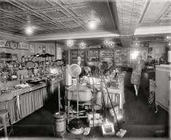 "Schneider electric store." C. Schneider's Sons in Washington, D.C., circa 1929. ("Give her an Electric Grill for Xmas.") Harris &amp; Ewing glass neg. View full size.
ABC washerGood info on the ABC washer but this model would have been a gravity drain -- the spout around the top of the spinner moved toward the washtub to redirect the water for reuse or into a sink or laundry tray/tub to dispose of.  The washtub had a hose that was lowered into a floor drain or bucket or a simple valve opened to drain the waste water out.
Quite a varietyThey even sold an electric mop!  It must have been a failed prototype, though, seeing as they're hard to find now.
CurrentI'm surprised they let all these AC appliances in DC.
Lionel TrainsBehind the man is a cabinet stocked with Lionel Electric Trains.  Today, that inventory would be a nice collection to have. Growing up in D.C. during the fifties, I could walk to three hardware stores that sold these.
Most Fascinating of AllIn a room of wonders for the period that would make it easy to wile away many hours of discovery and experimentation the most fascinating thing may just be the very up-to-date bare bulbs in the ceiling. These are an early version of todays ubiquitous yet now outdated "soft-white" incandescent bulb. Like the faces of both the man and flapper here photographed, all things, even with serious modernity, do come to an end.
Electricity in the airHe was madly in love with her, and she knew it. Look at her Mona Lisa smile.
Collector&#039;s Dream!As a collector of antique electric fans and related early electrical items, I feel like a kid in a candy store when I see pictures like this! 
Wonderful stuff Dave, thank you for putting all these great photos out for the world to see. It's almost like going back in time. Quite a few of us fan collectors check out your site daily looking for early electric fans which appear in some of the photos. 
Do you have any more shots of this particular store? I'd love to see different angles of all the goodies they had for sale.
[Alas, this is all there is. - Dave]
SchneiderI wonder if J.F. Schneider and Son Meats and Groceries was related to C. Schneider's Sons Electric store.
ABC WasherThe 2 tub spinner washing machine was first introduced by the Easy Washing Machine Corp. in 1926. This product differed from the wringer washers in that it had a  second tub with a high speed spinner that extracted water from the clothes. A simple drain hose hung over the sink or into a drain pipe. I think ABC was merged into or bought by Easy, the largest manufacturer of washing machines in the 1920s. The company was sold to Murray Electric (now part of Siemens) in 1957, and then to The Hupp Corp. Easy production ended in 1963. At its peak in 1948 the company sold almost 500,000 units.
No sunglasses?With nine bare bulbs, a tin ceiling and all that metal and chrome!
Sun LampIs that large lamp front center with what appears to be a transformer base a carbon-arc lamp? The box on the floor that would seem to go with it has a C and A on the end flap. Replacement parts?
[Letters on the box are U C. - Dave]
Electric Grill
C. Schneider's Sons
1207 F St. N.W.
Give Her An Electric Grill for Xmas
You Can Boil, Fry, Broil, Cook Anything
You Want in this Grill


It&#039;s not the ampsIt's not the amps, but the vamp who put the cat-that-swallowed-the-mouse look on the man's face. I think sparks have been flying in that room.  
What is it?What's the boxy device with the vented cupola next to the ABC washer (foreground, center)?
[An Eveready "Sunshine Lamp." See above. - Dave]
Circa 1929Thursday, May 2, 1929 to be exact.  Oh, and I'll take all of those electric trains in the display case.
Not for XmasMy father once gave my mother a waffle iron for Xmas. He spent a very cold night.
Advance of TechnologyYou can tell how better off we are today, our floor polishers are big or bigger than riding lawnmowers. The version next to the mop could not even hold a single drunk person.
Mystery ObjectOn the right of the picture, on the table behind the clocks (beside the serious-looking woman), in front of the calendar -- what are those round things that look like they have lights going all the way around?
[Light bulb displays. - Dave]
I feel like I&#039;m in a time machine.And just walked into this store with all these modern electric appliances. The detail is awesome, and it seems I could just ask either of these two a question about those cool little toasters. All these items would be very collectible today. 
Tick tock tick tockMy grandparents had the exact same clock as the "napoleon hat" shaped one to the right of the lady, and I still have a working flip toaster similar to the ones on her left.
I know a few people who would kill for one of those model trains in the cabinet at the back.
GE Monitor Top fridgeLove the GE Monitor Top refrigerator at the extreme right of the picture. Those things were built great, I myself have one only four years newer than this and it is still running perfectly.  
No GardenGee Dave, thanks alot for putting this great picture up at this time of year!  I have fallen in and won't come out until my garden weeds are six feet high!  The details have taken me hostage....will you ship me some squash come fall?
Coal miner&#039;s wifeI am thinking of the poor coal miner's wife which was posted
yesterday.  What a difference all these helpers would have
made for her, Another note. I still use a gooseneck lamp to read by. I have nothing better.
The bare bulbsIt seems that the several bare bulbs in the ceiling would have created a distracting glare. Wouldn't some sort of glass diffusers or shells have been available by this era? Perhaps they were so proud of their bulbs, they wanted shoppers to see them in all their unadorned glory.
On an unrelated note, the object the woman is leaning against looks sort of like a big-screen TV — an amusing illusion, to say the least.
Don&#039;t Try That TodayOr you will get the electric grill thrown right back at you upside the head.  Women do not want "household items" as gifts any more. This is a beautiful store, with a very nice looking couple running it and the lady with "sausage curls" was very well groomed for 1929. Lots to see here, thank you Shorpy for another photo containing many wonderful items to jog the memory.
Welcome!...To the Museum of Obsolete Technology! Where our motto is, "the more things change, the more they stay the same!"
Enough to curl your hairAnd somewhere in one of those boxes (front left, on the counter below the electric coffee pots) is the same model curling iron that gave her those perfect marcel waves.
Bask Naked in the Summer Sun"Boxy device" next to the washer is an Eveready Sunshine Lamp. More here.

Let me be the first to point outThe grammatical error in the poster near the top of the wall on the left.  That iron holds its heat, as well as one apostrophe too many.  On the other hand, it would make a fabulous gift!  Thanks for the suggestion, Dave.
ToastedI have one of those Edison electric toasters like the ones lined up behind the first one. Still works like new. It toasts one side at a time, so you have to turn the bread around.
I&#039;m a Little ... What?The appliance on the left -- Perc-O-Tea?
[Obviously you have never heard of the Perc-O-Toaster. And probably for good reason. - Dave]

Perc-o-ToasterWhat do you know, the Perc-o-Toaster seems to do exactly what its name implies! Here are a couple of more detailed pictures:
http://toast2go.tripod.com/ToasterGallery-Ads12.html
Make Mine Perky!I, for one, would love to own a Perk-O-Toast. 
Bare BulbsI live in a house built in 1925, we have that exact same light fixture in the hallway. It throws out precious little light even without the bulb cover, which is probably why someone removed it and put it in the attic. Probably the same case here.  For those who want to imagine, it's vaguely tulip shaped and made of white glass, you could find almost an exact replacement for it in any home improvement store today.
UnpluggedThe dustmop was obviously not meant to be in the photo. It isn't an electric appliance and has most certainly been used.
ABC and IThe washing machine is an ABC, which stands for Altofer Brothers Company. Henry Altofer, when he was a youth, built a crude  washing machine for his mother to make washday chores easier for her. It proved to be the beginning of the ABC company which grew into a major appliance manufacturer. A few years ago the old abandoned factory was still standing in Peoria, Illinois.
The Altofer and Gudeman families were close friends for many years. Henry witnessed the last will and testament of my great-grandfather Fritz Gudeman 10 days before Fritz died in 1890. Also, Henry and my grandfather David married sisters; and in 1936 Henry bought Fritz's old home and farm, located one mile north of Roanoke, Illinois, from one of his sons.
Hello Miss NewmanI had a phone call yesterday from a nice lady in Texas whose grandfather owned this store -- he's the man in the photo. Her father (who could be heard in the background exclaiming, "That's Dad!") identified the woman as one Miss Newman. He also recalled the pressed tin ceiling.
Dustmop Has a PurposeThe dustmop in front isn't a mistake. It's there as a sales tool. The store owner used it to demonstrate that his electric machine worked better at picking up dirt than a regular dustmop. That's why the mop appears to be used. It's the old Fuller Brush sales demo--throw dirt on the carpet and then show how the vacuum picks it up more efficiently.
On top of everythingThat ceiling has to be (well, I suppose it does not HAVE to be) the most ornately designed ceiling I have ever seen. I think it is unattractive. I wonder if our presumed-to-be-business-friends-only couple tried to avoid looking up at it, so as not to dampen the magic of their cramped but oh so electric moments together.    
Frozen in timeThis photo shows my grandfather Percy Christian Schneider in his store, which took its name from my great-great-grandfather Christian G. Schneider -- he began with a foundry that cast large items like bells, then moved into hardware. By 1929, C. Schneider's had become an outlet for the burgeoning appliance market.
Grandfather's assistant or clerk on the right is Miss Newman. My father, Donald Schneider, recognized his dad, Miss Newman and the store as soon as he saw the photograph. Thank you for preserving a little piece of my family's history.
Schneider ConnectionWould love to connect with Susie Schneider who left the last comment. I'm a long lost Schneider relative that is developing a website dedicated to our ancestors.
www.schneidersofdc.com
It's under construction.
Jon M. Schneider
Metal desk lampsI inherited one of those and tried to use it but the metal gets hot enough to burn the skin. Which is why my mother did not use it very often but it sat on the desk for years. 
(The Gallery, D.C., Harris + Ewing, Stores & Markets)
