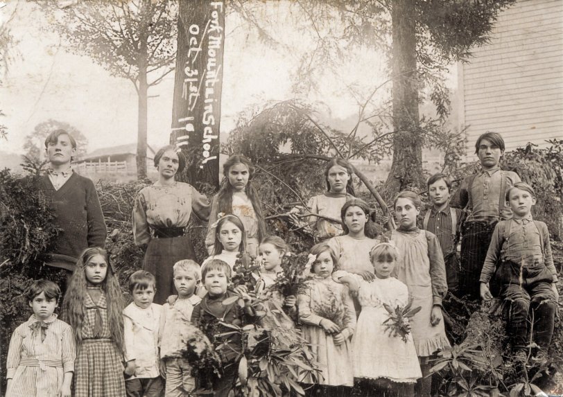 Fork Mountain School, West Virginia  (historical location), October 31, 1911.
Scanned from a silver/sepia print.
My grandmother, Myrta Shafer, all of 24 years old at the time, is the school marm standing by the tree, next to the girl who seems so intensely grim. I know that my grandmother was a teacher, and as I have been unable to identify anyone else in the photo, I assume that this was her class (my father, her oldest child, was not born for another six years).  1911 was the first year that costumed trick-or-treating was recorded in North America, so I doubt these rural children were preparing for a night of confectionery extortion. Perhaps their stolid expressions simply reflect their prospects, growing up in the devastated tinderbox that was Tucker County in 1911. View full size.

