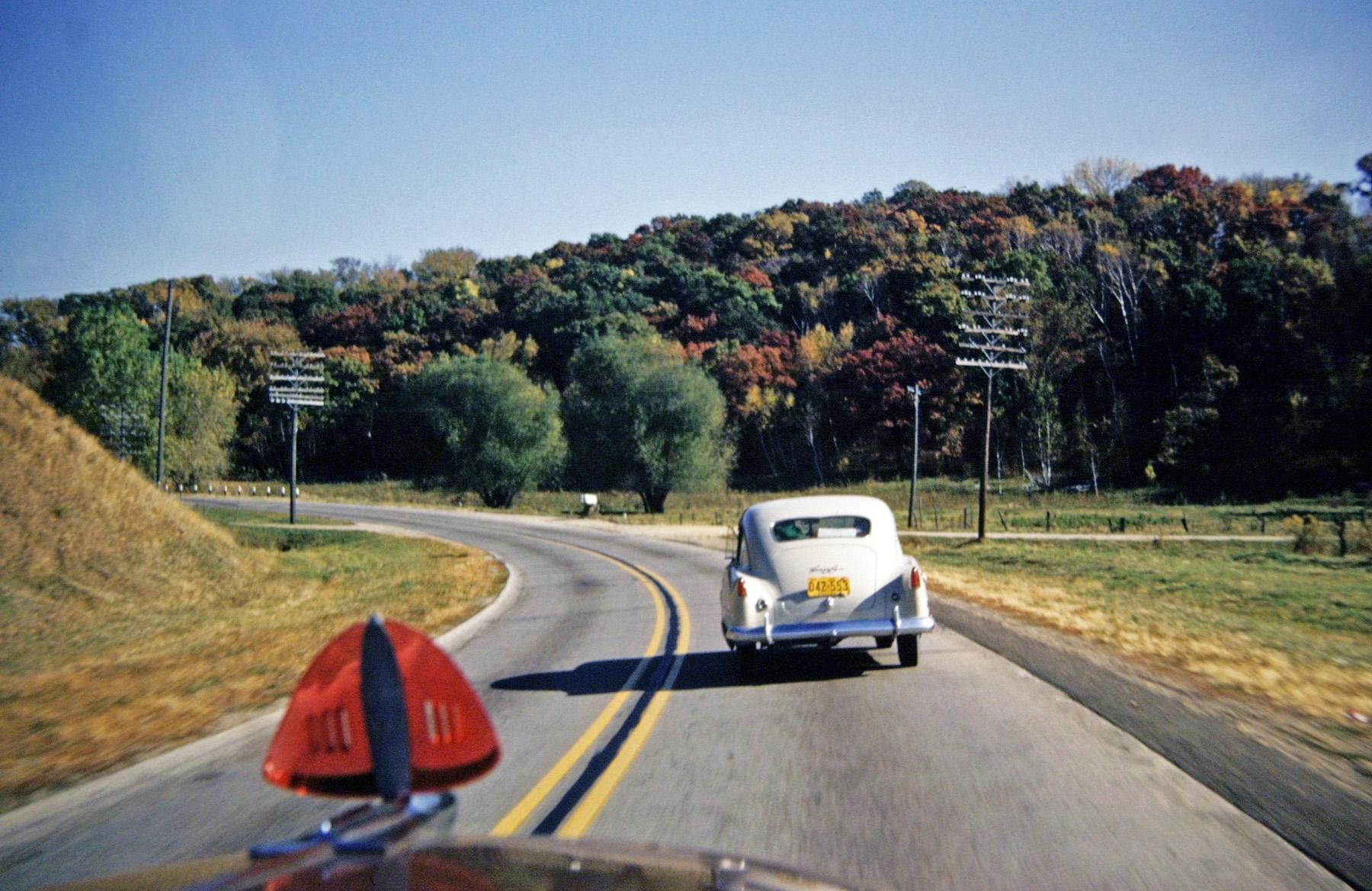 October 1953, on US 61 south of Hastings, Minnesota. The new Henry J with Wisconsin plates is flailing along on all four cylinders, but getting great gas mileage. We'll pass as soon as we get around this curve. Who remembers bug deflectors? View full size.