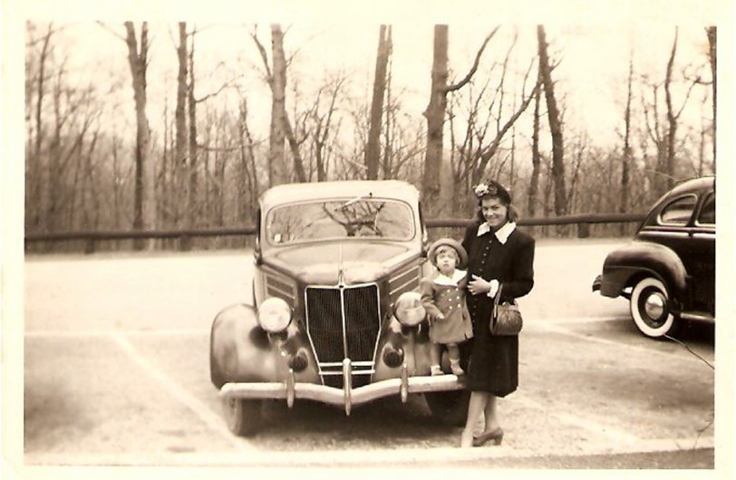 Long time Shorpy fan, first time post.  Came across the oldest photo of my grandmother and her first child that i've seen yet.  Location unknown but probably in Pennsylvania somewhere.  I'm curious if anybody can tell me what type of vehicle they are standing next to. Grandmother born in the roaring '20s, aunt born in the '40s. My guess is the vehicle is from the 40s. View full size.
