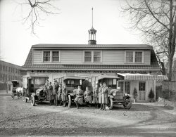 Washington, D.C., circa 1919. "Red Cross emergency ambulance station." National Photo Company Collection glass negative. View full size.
Left out?I wonder why the lady in the top left window wasn't allowed in the picture. She looks sad about it.
Red Cross Motor CorpsThe American Red Cross Motor Corps was first organised by Florence Jaffray Harriman and had about 45 members (mostly made up of women of independent means). Its garage at 16th and M streets was shown here in an earlier post.
The War and Navy department primarily used the service to transport war workers who had fallen sick, although in most cases it dealt with those suffering from the influenza pandemic of 1918.
UpstairsSomeone appears to be getting a timeout.
So much for my morningThese wonderful old photos that present something familiar in an unexpected way are my favorites.  I wonder how much productivity I'll lose this morning researching if The Red Cross provided standard ambulance care in our cities the same way they did on the battle fields.  The attire, the trucks, and now the research.
[Browse no further than this post, and in particular this comment. - Dave]
Grounded?Looks like someone didn't make it to the party.
Tank WagonWonder about the wagon partially visible. It appears to be a "tank car." There's what also looks like what may be a gas station. Huh. Could be connected.
[For another view click here. - Dave]
Those Atlas ambulancesseemed to be popular with the Red Cross.  They were manufactured by Martin Truck and Body Corp. of York, PA.  According to this item in The Hub for January 1918, 8 were delivered to the NYC Red Cross.
Remodeled?Is this the 16th Street station shown in other photos here? Same diamond pattern roofing, lighted cupola and striped awning but with a completely different roofline and dormers.
[This is an interesting question. Seems to be the same general location (same buildings to the right and in the background). Another version of this photo shows a 1919 license plate on the truck. Yet this image, with 1920 plates, and another image, dated 1917 and showing a 1918 license tag, both show the shorter building. Leading me to think there are two similar buildings in close proximity.  - Dave]
FluRemember, this was the height of the Spanish Influenza that killed so many people.  These volunteers are brave! 
Awesome BootsI spent 15 years in EMS and never had cool boots like that.
Red Cross RankCommonly misinterpreted as overseas service bars for duty in World War I, the bars on their left sleeves are actually rank insignia. The Red Cross had a rank system for nurses from one (highest) to seven (lowest). The rather matronly nurse on the far right, for example, would be described as a "Grade Four." No insignia on the sleeve meant they weren't fully qualified as nurses yet. 
MaypoleCheck out the maypole electrical pole camouflaged by the trees to the right of the house.
[Those are telephone lines. - Dave]
(The Gallery, Cars, Trucks, Buses, D.C., Natl Photo)