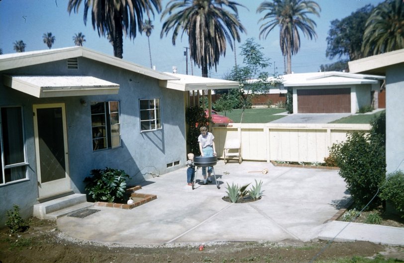 This is our backyard and patio in beautiful West Covina, CA about 1957. Mom and I are getting the BBQ set up for Dad. Those are agave and palm plants in the center of the patio, I think. The screen door leads to the living room. The window to the left of the screen door opens onto the dining room, where my family was having their Christmas dinner. View full size.
