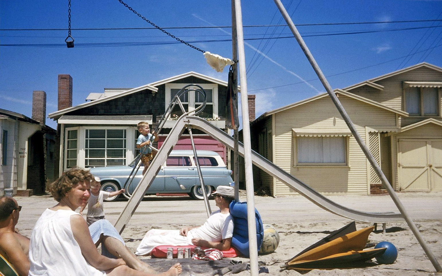 From circa 1958, a Kodachrome taken by my mother, who could handle a 35mm camera in a pinch. My parents had friends with a summer place in Seal Beach, California, a coastal community  on the border of Orange and Los Angeles counties. In the foreground are my parents' bosom pals who owned or rented the place behind the Ford station wagon. That's me at the bottom of the slide; the boy making his precarious way up is the son of the aforementioned couple. Dad (with the cap) appears to be zoning out, judging by the beer cans by his side. I wonder if any of these beachside homes exist today. View full size.
