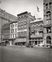 Washington, D.C., 1920. "National Radio School, Pennsylvania Avenue Northwest." National Photo Company Collection glass negative. View full size.
Republic of Chop SueyCan anyone make out the flag flying under Old Glory on top of the Chinese &amp; American restaurant?
Doubling upTwo Chinese restaurants in one block! One of them a walkup. And either two cigar stores, or one cigar store and a distributor.
Plus ca changeSo back then people paid to take "radio" classes like today they pay to take "computer" classes? 
You Street?I know that I Street in Washington is sometimes called "Eye Street," is "You Street" for U Street another common usage?  Never heard of it before.
Some nice details...- The guy cleaning windows on the 7th floor of the building on the far left. In all the Shorpy cityscapes I've looked at this is the first window cleaner.
- Two guys in hats peeping over the roof parapet of the Radio School.
- A man working in the Washington Post who is enjoying an open window. Looks like an editor from one of the 1930s newspaper films. The window he is sitting at has some nice architectural details and an unusual angled design.
- The Washington Post appears to share premises with the Cincinnati Enquirer.
- Nice devilish gargoyle and tessellations at the top of the Post building. Does it still exist?
- The parked car on the far left seems to have the letters CHEW on the trunk. I wonder what that meant.
["Don't Stay Behind -- CHEW Peper (something) Leaf." Tobacco salesman's car at the cigar store. - Dave]
Thanks, Shorpy for 15 minutes of interesting observation of another world. 
Look, up there!Who are the two men in hats on the roof of the Radio School building and what are they doing?
The guys on the roofPretty sure these hats belong to Stan and Oliver.
All goneThis row--even though some establishments sport Pennsylvania Avenue addresses--is actually on E Street, just east of 14th. The large building on the far left is the Willard Hotel. All the buildings here have been replaced a couple of times--currently the J.W. Marriott Hotel dominates this end of the block. Shorpy previously brought us a scene of a large crowd gathered to watch results from the big game at this same location in 1912.
[Before Pershing Park was built out in the 1930s, this block (lower right in the Baist map) was fronted by Pennsylvania Avenue. E Street is just to the right. - Dave]

View Larger Map
Re: Look, up there!Why, it's Barney and Gomer making sure the streets are safe from organized crime!
City of Chinese RestaurantsOne little known fact about 1920s Washington is that every other building back then housed a Chinese restaurant.
Radio RepairI think a lot of the classes focused on how a radio worked and how to repair them. In one of the antique radio repair books I read, the author recalled his father's studies in one of these schools. He later went on to become a radio operator on board a ship for a while. If I remember right, the book was Fixing Up Nice Old Radios.
[I think the focus was basically "getting into radio" from a technical and procedural standpoint, as Plus ca Change noted below. It was like the Web 15 years ago -- an emerging medium that was the Next Big Thing, and people wanted a foot in the door. This was just before the emergence of commercial radio as a mass entertainment medium, back when audio broadcasts were something geeky baseball fans listened to on headphone crystal sets, and the airwaves were thought of more in terms of wireless telegraphy and telephony, as a means of point-to-point communication, with an emphasis on maritime and military uses. - Dave]
Horse Apples!Need I say more?
National Radio Institute?I believe the National Radio School eventually become the National Radio Institute, who trained thousands of radio and television repairmen by correspondence until the 1990's.
Washington Post ManNewspapers have more than just writers and editors.  Plus, note that the window says "The Washington Post Business Office."  
Hence the man you can see in the window may be working in the circulation or advertising department, typing out bills, correcting invoices, or calculating how many papers are needed for that night's run based on subscription and street sales demand.
Learn WirelessCanton Pagoda, 1343 E St.
D. Loughran, 1347 Pa. Ave.
Oriental Restaurant. 1347 Pa. Ave.






Kronheim went into the liquor businessThe Milton S. Kronheim Company was a wine and spirits distributor in D.C. until going out of business in the late 1990s.
Perhaps the clothing business is what they did during Prohibition, or else once Repeal came in 1933, they decided to go into the alcohol beverage business.
+90Below is the identical view taken in April of 2010.  One can still get Chinese food by walking through the doors facing Pennsylvania Avenue, but it's a bit longer walk - the food court in the Metro Shops complex on F Street (the next street north) is accessible through this frontage.
(Technology, The Gallery, D.C., Natl Photo)
