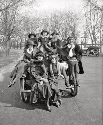 Washington, D.C., circa 1920. "Lanza Motor Co. -- Greenwich Village Girls." Somewhere under this mass of pulchritude is the Metz Master Six automobile. National Photo Company Collection glass negative. View full size.
Shoe envy!These gals look genuinely happy to be there! Love the girl in the back, I don't see her as graceless at all! 
Net ResultI'm glad that netting went out of style a long time ago. The women wearing veils here appear as either feline, at best, or suffering with some form of acne.
Greenwich Village GirlFront row left, gazing thoughtfully out to sea, seems to be the star of this photo, Bird Millman O'Day, a Ziegfeld and Ringling Brothers high-wire performer who appeared in the Greenwich Village Follies.
http://en.wikipedia.org/wiki/Bird_Millman
http://genealogyimagesofhistory.com/images3/Bird-Millman.jpg
Any One...of these veiled ladies could have her way with me.
NettingWell, if they're going to ride in a car like that, maybe the netting is to keep the bugs out of their teeth.
Metz Mistress SevenSo the Master Six seats Seven Misses.
Nice headlightsI'd like the lady on the bumper, to our right.  She reminds me of the Good Witch, Glenda.
&#039;TudeHey, "pulchritude," it's a nice word. It's been some time since I heard it. I'll think of using it once in a while.
The Metz Co.The Automobile -- December 9, 1915
Page 1051
The Metz Co., Waltham Mass., has placed on the market three types of delivery cars in addition to its roadster and touring car.  All are on a 25-hp, chassis , model A, having an express body selling for $475, with prest-o-lite tank and oil side and tail lamps. Model B is the same except that it has Gray &amp; Davis starting and lighting and sells for $525. Models C and D correspond to models A and B, respectively, except that they have roll side curtains, model C listing a $525 and model D listing at $575 model E uses the Gray &amp; Davis electric system and has a closed delivery type body. it sells for $600.
http://metzauto.wordpress.com/category/metz-company/
The Seven TopsOh, what a fun confection of hats. Although one must tsk at the rather graceless sprawl of the miss in the middle. I wonder if that came across as gauche and unladylike, or just a girl with her buddies having fun. (It's always so hard to tell who's at the age of accountability to the Powers That Be.)
Flapping>> I wonder if that came across as gauche and unladylike, or just a girl with her buddies having fun.
I think just fun. The 1920s were a great era of liberation for women in particular and youth in general. Pop culture (radio, magazines), peace and prosperity made for one rollicking decade.
General observation - Looking at all the pictures on this (excellent) web site - it strikes me that you don't see any obesity (save for that circus woman) anywhere.  
Fast food?  Sodas?  No smoking?  We drive everywhere now?
[Let's not forget "juice boxes." - Dave]
What a difference a decade makesCompared to the prim and proper ladies in our mysterious 1910 photo, these gals seem a century later in attitude, not merely 10 years.
For (an official) brief video on a recent show at the Galliera museum in Paris on clothing from the period 1919-29 "Les Annees Folles" (The Crazy Years), see here. Even if you don't speak French, you'll love the clothes. Emancipation!
Bald tires and pretty ladies.The tires back then. Were they supposed to be bald with no tread? Also. The girls look genuinely happy without hard eyes, a rarity today. I fell in love with top left gal very very pretty!
Body language.Front left. She is the one in charge.
Beautifully Adorned AutoI have never seen such a well appointed car, though you can't really see much of the car. If I could get my time machine working, I would have to pay that lovely young lady on the far right a visit.  I am hopelessly in love with her.
I&#039;m not sure if Mother would approveof the gal centre back straddling the hood. A "lady" still rode side-saddle in those days.
(The Gallery, Cars, Trucks, Buses, D.C., Natl Photo)