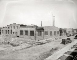 Washington circa 1920. "Sunshine Laundry." The new plant of the Arcade Laundry and Sunshine Dry Cleaning and Dyeing Co. on Lamont Street N.W. National Photo Company Collection glass negative. View full size.
Eternal Sunshine.Much to my surprise, the building is still there, and still looking pretty much the same.
View Larger Map
LOTWThose buildings are now the corporate headquarters of a commercial linen service called Linens of the Week.
 No Injurious Wringers 


Seeing Is Believing
Every Washington housewife is invited to inspect
the cleanest, largest, and sunniest and most scientific
establishment for laundrying, cleaning and dyeing
clothes in America - right in our own city.
The Arcade Laundry and
Sunshine Dry Cleaning &amp; Dyeing Co. Inc.

The Arcade Laundry and Sunshine Dry Cleaning &amp; Dyeing Co., is such an institution, the largest of its line in the city and one of the largest in America.
...
We want you to see and inspect the plant.  We want you to see for yourself the mammoth tanks where 55,000 gallons of water are softened each day, so that every lot of clothes is washed without rubbing in 700 gallons of water as soft as rain water, with seven changes of water to each lot.
You will be interested in the Mending Department, where all minor repairs are made without extra charge; the Individual Net Bags, where Handkerchiefs, Fine Waists, and Fancy Linens are protected; the Collar Ironers where even the edges are ironed, eliminating all roughness, the Clothes Extractors, which have replaced the injurious wringers.
...
You will see the finest of Silk Shirts, Dainty and Lacey Underwear being carefully Ironed by Electric Hand Irons.
...
In the Department of Dry Cleaning we will show you the plant for Naphtha Distilling, removing all grease and oil from naphtha and gasoline before being used.  You will see the Spotting Department, where all spots are removed by experts, each spot requiring different treatment, so as not to injure the fabric.
...
The Special Room for Dyeing is always of interest.  Here Outer Apparel of all kinds is dyed by our Guaranteed Process, without injury, even Rugs and Carpets, where colors are faded, can be made to look like new by a change in shade.
A feature of the Dyeing Department is made of a Special Emergency 24-Hour Mourning Service.  Families or individuals needing such service will have our undivided attention with every facility of this department at their disposal to prevent disappointment.

Advertisement, Washington Post, Nov 20, 1921


Outside the Plant"We want you to see and inspect the plant." Thus saith management, but if those invited housewives showed up, they might have had a few words to say about the plant yard.
[The plant hasn't opened yet -- it's still under construction. - Dave]
I must say that, as much as I appreciate the various landmarks of classical D.C. architecture Shorpy shows us, these old industrial buildings and plants are a special treat.
A matter of ScaleA question for photo experts: Why do these old photographs convey a much larger sense of scale than their modern-day equivalent? For example, when you look at Google street view of the Sunshine Laundry, the environment seems much smaller and more congested than the 1920 photo. I've noticed this with real life in-person comparisons as well; the first time I visited the Golden Gate bridge it seemed much smaller than in all the photos I had seen. Why?
(The Gallery, Cars, Trucks, Buses, D.C., Natl Photo)