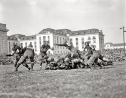 Washington, D.C., or vicinity circa 1920. The caption just says "football." Who can identify the venue? Harris &amp; Ewing Collection glass negative. View full size.
Mother BIsn't that Bancroft Hall at the U.S. Naval Academy in Annapolis?
Narrowing it downNavy played six home games in 1920, compared to just one road game (a 14-0 loss at Princeton) and their traditional neutral-site game against Army at the Polo Grounds in New York (a 7-0 victory.) These six home games were:
October 2: 14-7 loss to North Carolina State
October 9: 12-7 defeat of Lafayette
October 16: 7-2 defeat of Bucknell
October 30: 47-0 defeat of Western Reserve
November 6: 21-6 defeat of Georgetown
November 13: 63-0 defeat of South Carolina
[This could have been taken anytime from 1910 to the early 1920s. - Dave]
Next to BancroftOn the left it's either the Seamanship Building or the  Armory on the Naval Academy campus. As this 1919 panorama  shows, they were already bookends of Bancroft Hall and its yards. They're now known as MacDonough and Dahlgren Halls.

Go Navy!It's Bancroft, indeed. 
The shot is taken from the football field (now basically just a track), looking back at the "T" section of the rear wing of the dorm in the upper-left (which now has a 2-story walkway connecting it to the main building).
http://www.bing.com/maps/?v=2&amp;cp=qgxdyn8mssvt&amp;scene=25283264&amp;lvl=1&amp;sty=b
Beat Army!Swein is close, but I think you're on the wrong side of Bancroft. This shot is at Thompson Field, where Navy played their football games before the Navy-Marine Corps Memorial Stadium was built in 1959. It was situated where LeJeune Hall (the pool) and the 8th Wing of Bancroft stand today. The buildings seen in this picture are, I believe, the 6th Wing of Bancroft and, to the left, just the corner of Dahlgren Hall.
Love the stitched-on number patches. Would be interesting if anyone could figure out which game this was. The helmet "technology" seems to place it somewhere in the teens or '20s.
Back in the dayPeople talk about how violent the sport is today, but the 1909 football season saw 26 deaths on both college and professional teams during the regular season. This was more than double that of the 1908 season.
Navigation, please!!The photo is of Bancroft Hall at Annapolis but it's taken from due south of the campus. The corner of Dahlgren Hall is just showing to the far left and the sixth wing of Bancroft Hall is in the immediate background.  The fifth wing is in the far background.  The photo is taken from near what is today the site of Lejeune Hall. 
Action!The wonderful depth of field, the slightly skewed horizon and the players frozen in various athletic postures make this a superb action shot.  A great sports picture!
1922Based on a comparison to pictures in the Naval Academy's 1923 yearbook, this would appear to be Navy vs. Georgia Tech, 10/21/1922. 
http://media.scout.com/media/image/78/780837.jpg
Note #27 in both pictures.
1922, Georgia TechMike, thanks for determining the opponent! You made my day!
Perhaps Georgetown?Georgia Tech isn't listed as an opponent, but Georgetown is. And Georgetown wore uniforms similar to those shown in this photo. Examples here and here.
BTW, I love this site and have been working my way forward from the original photo of Shorpy Higgnbotham. I can't seem to get enough!
(The Gallery, D.C., Harris + Ewing, Sports)