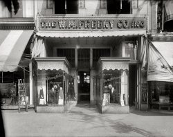Washington, D.C., circa 1920. "W.M. Freeny Co., front." The W.M. Freeny men's clothing store on 14th Street. National Photo Co. glass negative. View full size.
Flotsam and jetsamStrange that the photographer would have left that ugly ladder standing there to detract from his photo.  And what in the world is it that was won by the Police in 1917?  We'll probably never know......
I remember haberdasherieswhose well-trained clerks who worked in such fine stores supplying all manner of men's furnishings.  Harry Truman was one before he became president.  And they provided such good service that they would do free alterations to make your clothes fit perfectly, even if they were not custom-made.
And then, if you found clothes that would fit, you could go next-door to Velati's and stock up on famous caramels, bonbons, chocolates and pastries.
This was what a typical Main Street looked like when I was young and I must say, I found it much more personal than going into a cavernous super huge warehouse that sells everything under the sun, you push a massive, two-story shopping cart, walk a mile or more to find ALL your needs and finally take a number to check out.  Believe me young ones, some things were better in the olden days.
Mysterious LadderThat looks like an extension ladder for work in trees, or maybe street lamps. Fruit pickers had ladders like these, narrow at the top to make them easier to use in the branches, but it would work as well on sidewalk light standards. Probably not the photographer's. The shop window it's propped against (glass already cracked) looks like maybe the display window for a pawn broker. There's also a set of golf clubs and a croquet set in the window with the police trophy, and maybe a radio tuner. The odd array of giblets for sale isn't packed densely enough for a hardware or sporting goods store.
[It's the A.G. Spalding &amp; Bros. sporting goods store at 613 14th Street -- A.G. being Albert Goodwill Spalding of baseball fame. - Dave]
Velati CaramelsMy dad always said that if he had his life to live over, he'd live over a delicatessen. I might choose the Velati Famous Caramels shop.
Freeny lit upLooks like a warm late afternoon when this pic was snapped. I would love to have seen what the Freeny sign looked like at night, all lit up.
Shorpy viewers are the best!As soon as I saw this shot, I wondered just how quickly we'd know about the businesses on either side. You guys are just great. Thank you and Happy Fourth to all!
[More on Velati Caramels here and here. - Dave]
Sporting SpaldingAmazing detective work! So was this store part of a chain?
Where&#039;s the window cleaner?The ladder is very likely a widow cleaner's.  There are at least a couple of window cleaners here who ply there business walking from location to location, carrying their equipment including a ladder like this.
Albert G Spalding"So was this store part of a chain?"
Yes. Spalding Sporting Goods began when Albert Spalding opened his first sporting goods store in Chicago in 1875 or '76 with his brother. Spalding was a well known pitcher and by 1876 was playing with the Chicago White Stockings (now the Cubs) so his name on a store was going to drive traffic. Spalding published the first guide to the rules of baseball, and an annual Baseball Guide. By 1901 the store in Chicago had grown to a chain of 14 stores. Spalding died in 1915 but the company still exists, although not as a retail entity - it is Spalding Sporting Goods and produces balls for many sports - although as far as I can tell from their website, they no longer make baseballs.
(The Gallery, D.C., Natl Photo, Stores & Markets)
