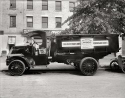 Washington, D.C., 1920. "Mack truck." As seen in the major motion picture "What's Your Hurry?," starring Wallce Reid as truck driver Dusty Rhoades.  National Photo Company Collection glass negative. View full size.
Mackin&#039;DC still had Mack garbage trucks with chain drive and solid tires in the mid-1930s.
JarringDriving this thing must have been a bone breaker, hard on the eyes (no windshield), a bear to control, and a lead-sled to stop. Pneumatic tires would have helped the ride a little.
MackosaurusWhat a dinosaur of a dumper. Chain drive, open cab and solid tires!
What&#039;s Your Hurry?Wallace Reid should have stuck with trucks.
After he was injured in a train wreck in 1919 while on location in Oregon making "Valley of the Giants," he was prescribed morphine so that he could keep working. He got hooked, and in 1923 died of an overdose.
In the stone ageof product safety - look at that open chain drive! How many fingers/hands/arms lost out to that beauty?
Big as a bread boxI've noticed these bread (pie, cake) lockers in some other Shorpy pics. I have read about bakeries making regular deliveries just like the milkman or ice man, and finally put 2 and 2 together -- these boxes are where they left your loaves, pies or cakes! What a fascinating detail of everyday life. It looks like this address also received deliveries of beverages from Reading Brewing.
Reading BrewingBelow, a 1912 "City Bulletin" from the Washington Post. To survive during Prohibition, Washington's breweries switched to selling low-alcohol beers, as well as various cereal- and malt-based soft drinks.
Legendary RideMy father, who was 16 years old in 1920, used to say of some cars, "Rides like a Mack Truck." It was never meant as a compliment.
Mack MaintenanceThe brakes on this Mack are on the rear wheels only. The brake band can be seen around the circumference of the large hub the small chain sprocket is mounted upon, the actuating lever from the foot pedal to the front of the brake hub draws the band tight.
To adjust the brake slack as the band wears, or after being renewed, the wing nuts below would be tightened or loosened as required.
To the rear of the small driving gear, inside the upper and lower chains, the slack adjuster for the chain can be seen on the hinging axle arm.
Threading the slack adjusters out on both sides will move the rear axle back, tightening the chain. Think of the chain on a single-speed bicycle, the rear wheel being moved back to tighten the chain.
The rear axle would have to be kept at right angles to the frame to prevent undue tire wear and the truck travelling straight rather than at an angle.
The much-larger driven gears can be seen through the spokes of the rear wheels.
The differential, normally between the rear wheels inside the axle housing under a vehicle is inside the frame of this truck, the two small chain drive gears on it's outer axle shafts outside the frame rails.
Heavy oil or chain lube grease would have to be liberally applied to the chain and the gears from time to time.
Eventually, wear from constant forward motion, sand and grit thrown up by the wheels, and chain stretch would wear the gear teeth and the chain would catch, or jump, and the gears and the chain would have to be replaced.
If a chain broke or jumped off the gears ( a la a single-speed bicycle again ) that wheel would no longer be driven nor have brakes.
The radiator on this model of Mack was behind the sloped engine hood between the engine and the dash.
The cooling fan was on the crankshaft behind the motor and blew cooling air out thru the rad cores and the louvers to each side next to the marker lamps.
On top of the rad is the radiator cap with a built-in thermometer often known as a 'Moto Meter' which had a thermometer that showed red inside a bulls-eye as the engine and rad water heat increased.
Operating a hard-rubber-tire truck over cobblestones, trolley tracks and bumpy roads would have been a real treat.
Driving this truck in winter ice and snow, even with chains, would have been a nightmare, and COLD.
Chain drive trucks, ( not only Mack marketed them ) albeit on pneumatic tires and with air brakes, were offered NEW into the early Fifties, their approach heralded by the rapid metallic clacking/buzzing sound of the chains gnashing around on their orbits. 
Another great photo on mechanics from Shorpy.
Thank You.
Nice!Mack trucks are from my hometown. I learned to drive a Mack just like that in the 70's, we had a 1912 but with a flatbed as a yard hack. It was a bonebreaker, you could only steer when it was moving. Oh god crank start was soo scary but kinda fun. No differential either, turning was crazy. No need for a windshield, it would not go faster than 20 MPH! and at that speed every bump and jolt was worse, it was like riding in an earthquake. Imagine trying to drive this beast, and having to manually advance the timing while steering, shifting, trying to stay in your seat and not crashing into anything.
Next in lineI see a beautiful piece of machinery. I'd love to look under the hood and take it for a test drive.
This old Mack.It's a nice pre-WWI, C-cab Mack AC. You can tell by the mesh covering the sides of the radiator. Newer models had louvers instead, plus a bigger radiator several inches wider than the hood.
Apparently this truck was recently painted for the occasion; I can see several dents and mends in the hood. Its original color would have been "Mack green," a dark and rather nice shade. The paint was lead-based varnish. 
Those trucks carried the gas tank inside the cab, right under the seat cushion, a-la Ford T. 
Optionally you could get a wooden-framed, two-piece windshield that bolted to the cowl and the underside of the roof. 
Also worth noting, they already had adhesive tape back in 1920, and they used it to affix the photo  to the sides of the cab. 
Turnbuckle stars!What? No one gets excited over architectural star turnbuckles anymore? Ach! You kids today!
Scared Me!When I was a small boy in the early fifties I used to play in a closed coal/lumber yard near my home. One morning I ran around a corner and head on into one of these HUGE Macks - it scared the bejeebers out of me! I have never forgotten the look of that truck.
Reid&#039;s AccidentEvery film book will tell you "Valley of the Giants" was filmed in Oregon, but it's just not true. The 1919 newspapers all say it was filmed in Humboldt County, California, and a review of the film--recently discovered in a Russian film archive--confirms it.
The St. Louis Post-Dispatch of August 23, 1919 mentions Wallace Reid's accident in a "railroad wreck scene which was so realistically produced that Reid was injured in it and forced to take a vacation which gave him an opportunity to visit St. Louis, his 'old home town.'"
(The Gallery, Cars, Trucks, Buses, D.C., Movies, Natl Photo)