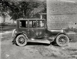 Washington, D.C., circa 1920. "Wayne Smith Auto Co. -- wrecked Haynes sedan." Out second glimpse at the operations of this long-forgotten car dealer. National Photo Company Collection glass negative. View full size.
Wow!The side airbags didn't even deploy!
Quite an ImpressionThe marks left in the side panels of this Haynes sedan clearly show just what happened. The other car's headlights and radiator, flanked by its fenders are easily seen. Classic T-bone collision. Now, could one of our antique car aficionados identify the culprit's make for us?  
Active restraints? What active restraints?Side curtain airbags?  Who needs 'em?  Why, in my day, we hit our heads against the windows, and we *liked it*!
It has to be saidThat'll buff right out!
Headlight printsVisible are what appear to be the imprints of the culprit's headlights and grille.
TotalledGreat Caesar's Ghost, there must be at least $50 in damage there!!
MKHNote the monogram.
That&#039;ll buff right outSince that car recently cost somewhere in the neighborhood of eight times as much as a Ford it probably didn't stay totaled for long, some enterprising fellow with a blowtorch and lead-paddles would've had it back on the road in short order.
Insist thatgenuine OEM Haynes parts be used to make the repair.
Three-door sedanIs this another attempt at just one door on the curb side of the car? I see what looks like the shape of afront door, but there is no handle or mounting point visible. This car did get repaired though, it obviously belonged to da Boss.
When is a Haynes not a HaynesI suggest the damaged car is an Oldsmobile, not a Haynes. A look at similar photos especially the hood of the Oldsmobile truck in an earlier Shorpy will confirm this. The fact that it is at a Haynes dealership is coincidental.
Wrecked By a Haynes?I must concur with the comment made by Hayslip that the cars is actually an Oldsmobile.  Maybe the Oldmobile owner was hit by a Haynes or traded the Olds in on a new Haynes.
The combination of extra glass panels on the side of the windshield, the tapering wheel hubs with a hexagon incised, the looped door handle, and the number of canted hood louvers all point towards a circa 1916 Oldsmobile.
A picture of another 1916 Oldsmobile is below.
Locus delictiThis appears to be the vacant lot across 22nd St. from the brand new Wayne Smith dealership. (Note rowhouse and empty lot at extreme right of that photo.) 
This also lines up with the 1919 Baist atlas, which came out a year before the Smith dealership was built &amp; thus also depicts that site (NW corner) as a vacant lot.
(The Gallery, Cars, Trucks, Buses, D.C., Natl Photo)