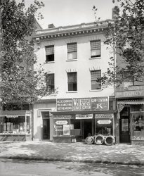 Washington, D.C., circa 1921. "Willard service station front, 1919 Pennsylvania Avenue." National Photo Company Collection glass negative. View full size.
Sign of the timesA Ford size Willard All-Rubber battery? Wouldn't a little lead and acid work better than rubber for starting a car? Of course if you only want to rent it for a day ...
The signs on this business are great. But I bet the place did not smell so great. Vulcanizing rubber stinks.
Embajada de MexicoNow the Embassy of Mexico.  The drug store is now a Starbucks. Usually I wish that you include the quadrant, not necessary to-day.
View Larger Map
View Larger Map
WhitesidesI'm more interested in the store to the left. They supply schools with cigars ... and drugs?
You couldhave your Willard serviced there.
Willard Storage Battery Co.A thumbnail history here:
http://ech.cwru.edu/ech-cgi/article.pl?id=WSBC
Barney Oldfield!When I was in my early twenties an older fellow I worked for  once accused me of driving like Barney Oldfield.  I blankly said "Who?" and the boss said, "Oh, I have dated myself haven't I?"  Apparently he had! I also didn't know he designed tires for Firestone!
Best smoked fish in townHenry's grocery store (on the right) survived into the 50s.  My mother took me there many times when we lived two blocks away.  (I especially liked the extension claw tool that the proprietor used to get merchandise down from the high shelves.)
(The Gallery, Cars, Trucks, Buses, D.C., Natl Photo)