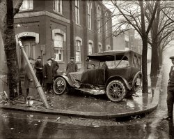 Another view of that 1921 car wreck at the intersection of 10th and R streets N.W. in Washington, D.C. National Photo Company glass negative. View full size.
Waffle House areaWell, the damaged street sign reads "10 ST" and if I could make out the sign on the building, I might have a better idea. I'm guessing NW and around Ford's Theatre (poss. where the FBI is now?).
[The building is a church. This could be 10th Street NW, NE, SE or SW. - Dave]
Corner of 10th and ?????Reading the crown of the street sign (to the left of the tree), it appears to be the intersection of
"10 ST" and _______?
The large building behind the car appears to be a church - note the arched shape of the windows and external buttressing. 
10th SEI'd say 10th Street SE.
SmilingIt looks like the driver is sort of smiling. He tore that car up! Imagine all this in age before seat belts and air bags!
[The two men in coveralls, including the guy in the car, would be from the wrecking garage. My candidate for the driver is the guy with the cigar. - Dave]
U Street, My CarFrom the wreckage of the lamppost strewn about I'd say the corner was either 10th and U Street NW or 1st and U St NW
The 10th Street intersection is just a couple blocks from the present day location of the U Street/Cordozo Green Line Metro Station. This was a very sketchy part of town in the early 80's - my Jeep CJ-5 was "partially stolen" near here in the last summer of the Carter administration. By partially stolen I mean someone hot-wired it and drove a couple of blocks away before abandoning it - either because it smelled so bad, or because it was such a heap of junk.
The 1st and U location is more probable because it looks more residential from Google Earth's perspective and in the photo. The building behind the wreck appears to be a  church, lodge, or some other public building - closely resembling a couple buildings near that intersection today.
I agree with Dave that the cigar-chomper is the driver - his eyes have that "adrenaline rush" look to them in both photos. 
[The sign says 10th Street. - Dave]
Yes, I see that now - looked like a "U" to these aging eyes. Still - some guy tried to steal my stinky car! Goob

Top Of The Pole?Look at what would have been the top of the toppled pole.  What is that cylindrical thing? Looks like a modern day surveillance camera. Was it a light fixture? Light? Traffic Light? Other?
[What it is is bent. In its unbroken state, the gas streetlamp would look like this. - Dave]

Church SignIt looks like there's a sign on the side of the church behind the group of guys, but I can't make it out.  Can you make it bigger, Dave?

Church SignYup, not enough to go on there.  Thanks for trying!
(The Gallery, Cars, Trucks, Buses, D.C., Natl Photo)