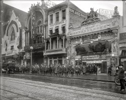 Washington, D.C., circa 1922. "Leader Theater, front." Sidney Lust's movie house on Ninth Street N.W. National Photo Company glass negative. View full size.
Into the MixWow. Interesting mix of dancehall cafe, Greek restaurant, vaudeville/burlesque house and cinema. Even in black-and-white, certainly more colorful than the mall multiplex.
Breathtaking ArchitecturePlease tell me this magnificent building is still standing. Built in 1910, it could be . . .please!
The gigantic statuary flanking the marquee---dwarfed by the HUGE roofline finial statues---is simply stunning. All the buildings along this block have unique architecture with intricate detail. Was this an "entertainment block"? I see a cafe/dance hall, burlesque house, the Leader theater, and a Greek restaurant. I wager to say even the "Washington Shoe Shine and Hat Cleaning Parlor" was probably an entertaining place to visit!
The Tarzan die cut advertising tucked around the marquee would be worth a small fortune on today's antique market!
The Port ArthurStarting from the left...



Washington Post, Oct 20, 1914 


Fight in Chinese Cafe
Three Men Arrested Following Row in
Port Arthur Restaurant

The moving-picture district on Ninth, between E and F streets northwest, was thrown into a state of excitement last night just as the shows were discharging their crowds by a fight in the Port Arthur Chinese restaurant, in which three young men are alleged to have attempted to smash everything in the shape of furnishings and the head of every Chinese employee in the place.
The trouble attracted a crowd that blockaded the street from curb to curb.  Cries and curses and the breaking of glass and tableware added to the situation.
Policeman Miller alone grappled with the fighters and emerged from the place brining three of the principles with him.  They were taken to the first precinct.
Morris Sing, proprieteor of the restaurant, told the police that the party came into his place and ordered food.  Then for some reason unknown one of the men picked up the dishes, smashed them, and then started a general assault principally against the Chinese employes of the place.
Several of the Chinese waiters were injured, but refused hospital treatment.




A one-sex audienceAll boys, I notice.  Apparently girls stayed home on Saturday afternoons.  All in knickers, scratchy woolen stockings and high leather shoes.  And every single one of them wearing a cap except the half-dozen or so who are holding them in their hands.
Helen Gibson in "The Wolverine."  Not much information, I'm afraid.
Elmo Lincoln in "The Adventures of Tarzan."  (Lots.)
The WolverineI had no idea Hugh Jackman was so old!
&quot;The Wolverine&quot;Plot Synopsis  	by Hans J. Wollstein
Based on a novel by the prolific B.M. Bower (pseudonym for novelist Bertha "Muzzy" Sinclair), The Wolverine starred former serial queen and stunt-woman Helen Gibson as a rancher who stands up for an employee (Jack Connolly) unjustly accused of cattle rustling. Ward Warren (Connolly) had come West after serving a prison sentence for a crime he didn't commit. History repeats itself for Ward when a couple of bandits he had chased off the land, accuses him of being a rustler himself. The former common-law wife of Hoot Gibson, Gibson (née Rose Wenger) had gained stardom replacing Helen Holmes in the long-running The Hazards of Helen. By no means a traditional screen beauty -- but spirited -- Gibson's starring career was brief, and she returned to stunt-doubling in talkies. 
http://www.allmovie.com/work/wolverine-117381
Around the World in a BlockThe architectural walking tour here is pretty wild. There's the Belle Epoque excesses of the Gayety and Leader theaters, crowned by their zinc copies of sculptures from the Petit Palais at the Exposition Universelle in Paris. Then there's the Gothic church facade of the Port Arthur Restaurant. And then there's the Acropolis (Greek) restaurant housed behind a Chinese balcony, left over from the Port Arthur's old location on the other side of the Gayety (the stairwell entrance to the "gothic" Port Arthur at 515-17 has a matching Chinese carved wood awning). But just when I was getting an urge for some nice spanakopita, I noticed that the Acropolis seems to have been replaced by the all-American Rowland's Buffet. 
Cable cars?Is that a cable slot between the streetcar tracks?
[It's access to the underground electrical supply that powered Washington's streetcars. - Dave]
&quot;Fastest Northwestern Picture Ever Screened&quot;What the heck does that mean?
["The Wolverine" was a train. Which is shown in the sign. - Dave]

Coming AttractionView Larger Map
The location today. The J. Edgar Hoover Building is right behind you.
The GayetyThis is right around the corner from the original 9:30 Club. I remember parking across the street from the Gayety in the early 80's. Creepy place, they showed "adult" movies. Lots of drug addicts and perverts.
Wilbur Mills and the GayetyThe Gayety lasted into the 1970s.  That's where House Ways and Means Chairman Wilbur Mills first met "Argentine Firecracker" Fanne Fox, who later jumped from his car into the Tidal Basin and sank Mill's career.
Gorgeous photograph!And also a revelation for me. Was The Port Arthur a Chinese food chain? There was also one by that name in downtown Providence. I don't know when it opened there, but I do know that it lasted well into the 1940's and was - according to my Dad - the hottest place to go to on a Saturday night in the late 30's and early 40's. Drinking, dancing to a band and exotic, for its time, Chinese food.
My Aunt Mary and another female relative sang there, as well.
What an eye-opener! And what a thrill this photo is to drink in! I'd throw down my nickel to see that movie in a second - if only for the pleasure of getting to see what the inside of the theater looked like!
This is one of the very best postings this year.
[Below: The Port Arthur Chinese restaurant in New York. Click to enlarge. - Dave]

Helen GibsonThat picture is awesome.  Thanks for sharing it.  I have been researching Helen Gibson for many years and have many of her personal ephemera pieces. Including her copy of the Wolverine lobby card with the image enlarged as a poster on the left of the entrance. Thanks for your site, I always see something exciting.

Newsboy MatineeGiven all the young boys and the fact that that whatever is going on here it merited a photograph, I am guessing this is another gathering of newsboys for a Saturday matinee.  Shorpy viewers have previously seen a similar event in this 1925 photo of the Leader Theater.  Alas, no sign of Bo-Bo, "the monkey with the human brain," in the photo.



Washington Post, Feb 12, 1922 


Carriers' Theater Party

Many Post newsboys yesterday had the time of their lives at the showings of the latest installment of the Adventures of Tarzan at Sidney B. Lust's Leader and Truxton theaters as the guests of Mr. Lust and the circulation department of the Post.  The boys found the day an even greater event than they had expected, for in the morning at their homes, each had received letters from W.C. Shelton, circulation manager of The Post, thanking them for their efforts delivering The Post on time during the storm and enclosing $1 as a bonus.
Mr. Lust, who was host to a number of the carriers yesterday, will entertain as many more today, for tickets good for either day were sent out.  As a special inducement to efficient service, the boys who rank among the best carriers in the city will receive free movie tickets for the next 15 weeks.
The boys had been particularly interested in the Tarzan film, which features Elmo Lincoln. Bo-Bo, the monkey with the human brain, was on hand to meet the boys when they reached the Theater, and on leaving every boy was given a bag of peanuts.  Bo-Bo plays an important part in the Tarzan serial, and his antics created much amusement.

Elmo!Where else but in America could a guy named Elmo with a 52-inch chest become a movie star? In addition to his rightful claim to fame as the first film Tarzan (in 1918), Elmo Lincoln was also in the silent classics  "Birth of a Nation," "Intolerance" and "That Fatal Glass of Beer." He came back in the late 1930s in bit roles in talkies, including "The Hunchback of Notre Dame."
"The Adventures of Tarzan" was Lincoln's third and final foray in the role of the vine-swinger, which was probably just as well, as he was afraid of heights. Released as a 15-part serial, it was one of the smash hits of the year, taking in more than Valentino's "The Sheik."
Sugar Plums at the GayetyWhen this photo was taken, burlesque had not yet begun its long slide from musical comedies and revues into adults-only sleaze. The Washington Gayety was one in a large chain of theaters, with shows rotating among them on a circuit, as in vaudeville. Gayety shows featured such stars as Al Jolson, Fanny Brice, Sophie Tucker and Will Rogers. Harry Coleman, starring in the Washington Gayety's "Sugar Plums," was a comedian who began receiving favorable reviews around 1915, and appeared in a few silent films as early as 1910 (his last film credit is as a bit player in the dance hall scenes in Chaplin's "The Gold Rush"). On Nov. 8, 1918, the Toronto World ran a notice for the Toronto Gayety's new show "The Roseland Girls," beginning with this lead:
"The Roseland Girls" is a show that may always be relied upon to furnish the sort of entertainment that the patrons of the Gayety Theatre will like and will be enjoyed by all classes of theatregoers. The company is headed by Harry Coleman, Bert Lahr, Kitty Mitchell" [and others].
Absolutely wonderful. What a civilization we once had!
The adult on the far right appears to be halting traffic with his blurry arms so as to give the photog a clear view of the newsboys.
Elmo of the ApesElmo Lincoln was in the first Tarzan feature, "Tarzan of the Apes," which was filmed in Morgan City, La. (I suppose if you took the Southern Pacific east out of LA that would be the first quasi-jungle swamp you would come to.)
Morgan City is a real pit, an oilfield blue collar town with not much going for it.  In 1986 I was staying overnight there and read in some chamber of commerce brochure an invitation to come back in 1988, for the 70th anniversary of the release of the film and Morgan City's Tarzan fest.
Two years later the Wall St. Journal had an article in its humorous-story corner about how in the midst of all the planning the Edgar Rice Burroughs estate prevented Morgan City from going forward with the festival.  The poor town was stuck with all of the preliminary costs of their big event in the city's history.  What a shame.
Good thing there was a captionI couldn't see the name of the theatre anywhere on it.  I suppose it could be covered by a banner for the movie.  You'd never see a business today allowing its identity to be obscured.
Elmo Is My HomeboyElmo Lincoln is the only movie star from my hometown of Rochester, Indiana!  That's all I've got to say.  Some 4-digit population towns can't claim ANY movie stars.
What is next door?Does anyone read Greek?  I wonder what the upstairs of the building on the theater's left houses?
[The name is there in both Greek and English: Acropolis Cafe. - Dave]
Dressed to the NinesI can't imagine a group of that many boys wearing ties to a movie today.
(The Gallery, D.C., Movies, Natl Photo)