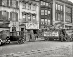Washington, D.C., circa 1922. "Amalgamated Tires, 14th Street N.W." Hurry on down for our BIG SALE! National Photo Co. glass negative. View full size.
In the History of TiredomWhat a cruel irony that the truck carrying all those nice, comfy pneumatic tires is still rolling on solid-rubber tires.
Tire InflationI just bought new tires for my SUV at $250 per.  I checked an inflation calculator and $10 in 1922 is about $125 today, and $20 is about $250.  Seems the more things change, the more they stay the same.
How can you afford to slash your tires in half?"Easy. We're selling them at half price!"
6000 mile guarantee!The "firsts" have a 6000-mile guarantee. I wonder what the guarantee of the "seconds" and "thirds" might be.
Also, the best tire sign I've seen advertised a "huge tire blowout." I chose another shop.
Non-Skid TiresAs opposed to what -- Goodyear Slip-N-Skids?
Amalgamated? I always buy from Acme.
Stop! You&#039;re under arrest!... for savings!
Portage Cords and Fabrics


That fifth man ... is a reflection of the fellow holding the tire.
Another Center Door!And another center door Model T! Love the car pictures!
The 6,000-mile guaranteeWasn't as ludicrous as it appears today.  People generally didn't drive that much back in the 1920s.  From what I recall reading, the average was in the 2,000-3,000-mile range.
The fifth manMy favorite part of this photo is the fifth man, hiding (or so he thinks) behind the car on the left.
Absolutely, positivelynot there anymore.  Across the street from Franklin Park, a footbeat of my youth.
Tire Inflation not the same.$250 today is a GREAT buy. Your new tyres today have a life 60,000 miles. The tyres from 98 years ago lived only a tenth of that. Better materials, better engineered, and much better ride quality. 
Wow.Those two men in the middle remind me of my brothers Bill and John.
Super LOW Profile35-5's I bet!
Chains Next DoorI am curious about the pair of chains descending from the mailbox-looking protrusions on the building to the right of Amalgamated. Can't quite figure out their purpose.
[Seems to be a chain hoist, the kind used for window-washing platforms. - Dave]
Center Door SedanMy dad had a 1920 Ford center-door sedan.  A fairly unique car. The driver entered through either door and had to go between the front seats to get into the driver's seat.  The side windows were raised and lowered using a fabric strap.  The gas tank was accessed by lifting the cushion of the driver's seat and removing the gas cap.  You checked the gas supply by dipping a wooden stick about the size of a paint stirrer with graduated markings.  To add gasoline, the hose was brought in through the driver's window or the passenger door.  His car was painted up as a Black &amp; White Taxi for the film "The Court Martial of Billy Mitchell," which was filmed in D.C. in 1955, starring Gary Cooper. The NON-SKID tires made by Firestone had those words as the tread pattern.
Re Center door sedanHiggins said: "The side windows were raised and lowered using a fabric strap." Chevy's ultra lightweight 1963 Grand Sport Corvettes (only five were built of a planned 125 intended for a factory racing program that was scuttled) had the same device to raise and lower their plexiglass side windows. The straps had a number of grommets which allowed the driver to position the windows at several openings with a hook on the door below the window opening. This arrangement of course saved a few very critical pounds by eliminating all the window winding hardware.
(The Gallery, Cars, Trucks, Buses, D.C., Natl Photo)