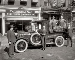 Washington, D.C., circa 1922. "Minker Motor Co., 14th Street N.W." National Photo Company Collection glass negative. View full size.
Lotsa nice detailsThis is one of the finer Photographs. I notice the guy in the middle didn't notice to fix his pant cuff. The mechanics seem to be paper cutouts. I'd guess it's because of some combination of depth-of-field and lighting. And what does it mean when even a mechanic wears a necktie?
Still thereView Larger Map
Interchangeable WheelsNote the gear teeth on the inner hub of each wheel.  I believe this is done so any wheel can replace the wheel that drives the speedometer gearbox. I see the side-mount spare is locked to its mount: technology changes but people don't.
How odd compared to todayHas anyone ever seen Boston ferns in the front window of ANY automobile dealership? 
Shoeshine AnalysisI have always thought that, back in the day, men took pride in having well-shined shoes.  Of the three men in suits standing in front of the truck, the one on the left, who has the best suit, seems to have at least the remnant of a shine, the guy in the middle looks like he dug ditches in those things, and the guy in the rear with the straw boater has a badly fitting suit, but at least a decent shine. Wouldn't a car salesman taken a little more care in his appearance?
Blue Collar NecktiesI had a friend who worked as a plumber on new construction jobs. He always wore white shirt and tie under his coveralls at the site. He said that many of the guys in construction also wore them, they kept the cold out.
CharactersSome interesting chaps in that photo, and an interesting truck; good fodder for interwebz research.
Hey!  What is Al Capone doing in the photo?
Columbia Dump Truck? Columbia, which built cars from 1916 - 1924, never made trucks, but this is definitely a Coumbia based truck.
This appears to be a 1917 - first half of 1922 car that has been converted to a truck.  Columbia's hood, hood sides, headlights, and radiator/grille remained the same during this period of time so a more definite dating would be very difficult.
That being said, the running board and fenders do not look very beat up; however, it would have been fairly easy for a Columbia dealer to replace damaged originals. 
The front and rear tires are are of two different makes (a pretty bald Beacon and a slightly worn Lehigh).  Look at the tire on the running board for comparison (also a Lehigh).
The windshield has been modified to stand straight up.  On Columbia open cars this is normally tilted back.  Note how the top posts for attaching a convertible/folding top are pointing forward instead of pointing straight up as shown in Columbia photos and brochures.  The piece that extends from the bottom of the windshield to the top of the cowl is missing.
Is this a dump truck?  There is a round cutout in front of the rear tire about the running board.  This looks like it is for attaching a crank handle to raise the bed/body of the truck and dumping a load.  It could also be for a power take off (PTO) to run another piece of machinery.  The man in front of the cab is blocking the view that would help to determine if the cab lifts with the bed.
I think it is a dump truck.  There is a fairly wide gap running through the cab from behind the man to the cabs right hand side.  There is also a cross beam that extends to the very edge of the cab under the number "14th" painted on the body of the bed.
I imagine that originally this was a Coumbia touring car that was in an accident,and they rebodied it to make a service truck.
The wire wheels were a $100 Columbia option.
The rest of the storyAt least about the building, not the actual company: here.
(The Gallery, Cars, Trucks, Buses, D.C., Natl Photo)