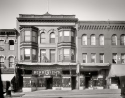 Washington circa 1921. "Berberich's, Seventh Street." The Berberich store at 1116-1122 Seventh Street N.W., "Washington's most progressive shoe house." National Photo Company Collection glass negative. View full size.
I &lt;heart&gt; DCThere's no question that the loss of these historical buildings is a tragedy.  But, there are still many buildings like them all around DC.
The city went through a period where many neighborhoods were more like slums and the houses were is such great disrepair that it would have been prohibitively expensive to renovate them.
In fact, when tax relief for investors seeking to renovate houses in DC was enacted, we all eventually benefited.  That's where the "live in the house for 2 years and pay no capital gains on the profit (up to a certain amount)"  comes from.
And to truly renovate a house like one of these in some cases required hollowing out the whole thing and starting from scratch.  You could save the carved moldings, but many of the houses predate wiring, ducting, etc.  And the roofs would be in bad shape allowing for water to get inside and the mold problem would be terrible.
They almost tore down the Willard Hotel in the 80's for gosh sakes!  It is one of the most beautiful architectural structures in the city! (Not to mention a very nice hotel.)
And there is a "feel" to the city that you can only get by going there.  These pictures, for me, are an enhancement.  My father worked in the city for over 35 years--my parents met there.  I was married there.  The bustle of the traffic, the gravity of the stone granite federal buildings, the many different periods reflected in the architecture are a treat to the senses.
Are there buildings that are basically ugly brick boxes?  Yes.  There are also interesting buildings from the 60's and 70's.
Personally, I love the city in winter.  Maybe because I was married there in the winter at St Dominic's and honeymooned at the Shoreham.  But, it's not like New York or really any other city.
For one thing, the buildings tend to be shorter -- especially in the Federal Triangle.
And visiting the various museums is a real treat.  There are parks here and there that kind of surprise you--beautiful parks.  And the area by the zoo is old and beautiful.  The college campuses are also gorgeous.
There really is more than "seeing" DC.  It is an experience.
These pictures enhance my experience of the city.  And while I mourn that many of these buildings are no longer there, there are plenty that will be there long after all of us are gone.
Mme. BelleMme. Belle is not the first palmist to appear at Shorpy.  We have previously seen signs for Mme. LaBey and a glimpse of Mme. Trent.



50c &nbsp; &nbsp; &nbsp; &nbsp;  MME. BELLE &nbsp; &nbsp; &nbsp; &nbsp;  50c 

Egyptian palmist, gives true advice in business, love, health, and family affairs.  Confidential readings daily, 10 a.m. to 8 p.m. 1124 7th st nw., between L and M sts.

Advertisement, Washington Post, July 22, 1921 


ManageableI miss the days when cities were manageable. When your neighborhood had the butcher, the baker, the shoe and clothing stores. You could walk to them, or take the trolley. I grew up in San Francisco in the late 1930s-40s, and these photos remind me so much of what was there. Of course in those days, there wasn't so much to buy, and we didn't "need" to buy so much. 
There&#039;s Nothing There Anymore ...Except "modernization" and general, all-round nothingness. One of the real downsides to visiting this website is that, although I've never been to Washington, D.C., I cannot think of any reason to ever want to go there. I feel like I'm seeing the best of it here -- and Google Maps is filling in the rest of the sad, sorry tale.
Progressive ShoesAt last, a really progressive shoe purveyor, a welcome relief from the myriad reactionary footwear specialists!
Lower left corner...I love these little glimpses - the man at the truck looking at the blur of a passing woman on the sidewalk!
The "scientific" palmist the only window open with fluttering curtains, the flat top windows on the second floor and the arches on the third, in both buildings, and the sunburst iron railing design, et cetera.
I wonder why so much of Washington, but still they are interesting!
[Aren't they indeed. - Dave]
Today, the Convention CenterView Larger Map
Shoe Store Post OfficeThose were the best of times.  One simply cannot find a good shoe store/post office anymore.
Lovely buildingBerberich's may have been an everyday shoe emporium, but its building was delightful. It's amazing the detail that brick and stone masons of the day put into their art (and architecture) for simple, business buildings that were torn down later without a thought or a care. I liked the multitasking the photo reveals, too: Shoe store and postal station. Please note that Mme Bell was a "scientific" palm reader!
Mme BellI wonder if "Mme Bell, Scientific Palmist," knew that her office sign would appear on Shorpy someday.
What a marketing move!Go to the Post Office and see the latest in shoe wear. You know you can't tell your wife not to go to the Post Office!
ManageableAnon sed: "I miss the days when cities were manageable. When your neighborhood had the butcher, the baker, the shoe and clothing stores."
There are many of those smaller, manageable cities thriving still across our wide land. I share your sentiment and will leave the greater LA area when I retire to Oregon -- to one of the cities for which we both pine.
Via this post, I consider the trout in streams neighboring that manageable city to have been formally warned.
Berberich&#039;s

The Fortieth Birthday of Berberich's Shoe House
Started with Nine-Foot Front, Now Has 12,000 Square Feet Floor space.

...
Just forty years ago Robert Berberich opened a small store at 1118 Seventh street northwest.  This store was only nine feet wide and less than thirty deep.  A large part of the business done at first was made-to-measure work.  Mr Berberich, who was an expert shoemaker, fitted and sold to the best people of that period their boots.  He soon gained a reputation for style and high quality work which has followed him even to this day.  Although he is now retired and leading a quiet dignified life, he watches with much pleasure the prestige which his two sons, who have succeeded to the business, are enjoying, knowing that they are reaping the benefits of the lucrative business of which he was the father.
From that small nine-foot front beginning the firm has grown until today it occupies 12,000 square feet of floor space of which 4,000 was recently added.  The little nine-foot store was in a little frame building, but this was then one of the landmarks of the city, and was known as Berberich's - Seventh street being the busiest thoroughfare in Washington.  Mr. Berberich was one of the pioneer merchants of this thoroughfare. Taking a just business pride, he soon outgrew his cramped quarters, and owing to this continually growing business he was forced to a larger more modern store.
He then bought the property at 1138 Seventh Street, this being in 1877, only nine years after the business began.  At the time Mr. Berberich purchased this place it was a small frame building, set on a steep bank.  After bringing this down to street level, he built upon the site a three-store brick dwelling, 25 feet front, at that time considered a handsome modern building.  Here with 1,500 square feet of floor space and his store fitted up in the best manner, his trade continued to expand. ...
In 1902 the firm, which by this time included the two sons, Robert J. and Joseph A., purchased the property at 1116-1118-1120 Seventh street, of which the original store was a part.  On this site was erected the handsome building which no adorns the neighborhood, and is the best appointed of the modern shoe stores in the city. This new store was fitted up in the most modern way, the best grade of oak being used for shelving with quartered oak and grill work decorate them in a proper manner.
In the rear of the store are three of the largest mirrors in Washington, which take up the entire back wall and give the store the appearance of being several hundred feet deep.
...
Only a few months ago they added the property adjoining them on the north, numbered 1222, to their store.  This now gives them from 1116 to 1122, a total frontage of 60 feet.
[Article goes on to detail the many brands of shoes carried by Berberich, many of them under exclusive contract for Washington: Buster Brown Blue Ribbon Shoes, La France Shoe, Selz "Royal Blue," Burt &amp; Packard "Korrect Shape," and American Girl Shoe.] 

Washington Post, Sep 20, 1908 


In 1927, Berberich's closed their store at 1116-18-20 Seventh street and relocated to Twelfth and F, northwest.
[And filed for bankruptcy in 1931. - Dave]
The Old MathIf this business opened 40 years before 1921, then it opened in 1881.  In the article below, however, it states that "in 1877, only nine years after the business began." If the 1877 date is correct, than the company opened in 1868.  Am I missing something here or do we have a case of "alternative" math?
[You're missing something. The article is from 1908, not from 1921. - Dave]
Robert Berberich and Son’s Shoe EmporiumThat’s my great-grandfather’s shoe business there.  Amazing, what an incredible
historical building and era…
Carole
(The Gallery, D.C., Natl Photo, Stores & Markets)