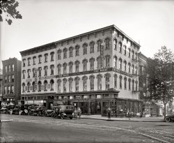 Circa 1919, another Washington streetscape. "The Mode, 11th and F Streets." National Photo Company Collection glass negative. View full size.
Oh, that reminds me...I gotta pick up a couple of hat frames tomorrow.
Do you suppose ...that some of the ghosts in this picture would have been virtually invisible if they hadn't chosen to wear shoes that day?
Hatter and haberdasherNow what is the difference between a hatter and a haberdasher? I had always assumed they were the same.
[Hatters and milliners do hats; haberdashers do haberdashery -- men's clothing and accessories. - Dave]
Baked Possum TodayThe United Cafeteria opened in February 1919.  The ad below is for one of their more exotic dinners.  Based on other advertisements, the more typical fare included Roast Prime Ribs, Oyster Pot Pie, Chicken A La King, and Lobster a La Neuburg.


A Success From the Start

Washington during the past week has given cordial welcome to the United Cafeteria, 1008-1010 F street, opened a few days ago as the latest addition to the National Capital's already noteworthy assemblage of dining places.  The new restaurant is unique in many of its features.  A woman chef superintends the appetizing conceits that proceed from the kitchens to the display counters, patrons are taken care of at double capacity service stations and a stringed orchestra is regularly in attendance.  A palm room is the novelty that occupies the basement floor.
Every appointment of the spacious dining rooms, from the immaculate linen to the generously filled platters, is suggestive of the refinements of service not ordinarily afforded by dining places of the popular, quick-lunch type.  Courtesy, promptness and thoroughness of service, together with every excellence of cuisine, have united to command a patronage of over a thousand patrons at every meal.  To Richard Neddo, president of United Cafeteria Company and owner of Hotel Neddo, of Norfolk Va., is accorded the praise for the enterprise that gives Washington this new and commodious and altogether desirable place to eat.  It's the crowning achievement, by the way, in the career of a man who as a train boy received his first "service" lessons in dispensing water to travelers on the old C.H. and D.R.R [Cincinnati, Hamilton, &amp; Dayton Railroad] back in 1873.

Washington Post, Feb 9, 1919




Boccioni Anyone?Look at the couple crossing the street and behold the vision that inspired the Futurist movement.
Still thereThe Mode is gone, but not the two fine red brick buildings behind it on 11th.
View Larger Map
Even back then...you couldn't find a parking space in D.C.
Possum PieI've heard possums described in many different ways, but "the sweetest morsel that can be set before man" is not one of them. I wonder how many hungry customers showed up that day?
Nice ridesA couple of expensive cars here -- can't identify the town car in the center, but the one with the light colored wheels to the left is a Pierce-Arrow.
Scarred and batteredThis building was sadly maimed before it was razed in the mid-90s - it's visible at far left here:

image from Flickr user Kinorama.
+90Below is the identical perspective taken in September of 2009.  The Mode building was a pretty pathetic site in its last years on that corner.
(The Gallery, Cars, Trucks, Buses, D.C., Natl Photo, Stores & Markets)