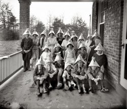 "John M. Bear Jr., 11/26/22." Twenty-one little kids. All wearing hats decorated with characters from the funny papers. At Johnny's 11th birthday party. And they're  mortified, every last one. (Thought you'd all slip under the radar, did you? That this embarrassing little artifact would just go on collecting dust at the bottom of a box somewhere? Well. Guess what. Not only did they invent radar, they invented computers and scanners and the Internet. Bwahaha. View full size!)
See You in the Funny Papers!They're all adorable.  Check out the vampette in the Jerry hat playing peekaboo with her ostrich feather fan.  Standing left is Jeff who is thinking, "This is nowhere near as much fun as The Mark of Zorro."
Kids Love Boob!toonopedia has the scoop on most of these characters.
Boob McNutt started as a series of one-shot gags, which usually ended with Boob being tortured to death for his innocently destructive ways, but before long, week-to-week continuity was added. In 1922, he met the love of his life, Pearl, and the focus shifted to his quest to win her hand in marriage. The task was accomplished in 1926, but they were soon divorced. They went through a few more cycles of courtship, marriage and divorce.
Funny Cartoons...I'm not sure you could have a character today called "Boob McNutt"... Great shot...
Sheesh.Never has fun looked so enforced.
Attn. Internet: Please pick up your shipment of WINHo. Lee. Mo. Ley. What an amazing picture. Although I do have to wonder how much counseling the kid with the "Boob McNutt" hat had to undergo later in life.
Gloomy GusFabulous picture!
Check out Gloomy Gus there in the middle. Her little moniker suits her just fine, don't you think?
Next to her is "Boob McNutt." *snicker snicker*
And the row of preteen girls in the back. Oh, can't you just feel the awkward?!
I'm guessing the adult responsible for this is standing to the right of the kids. Many of them are looking that way with looks on their faces ranging from disbelief to possible hatred. But mostly disbelief.
Now Stop It, All Of You!My guesses on why the long faces include the probability that they've just been threatened with bodily harm into keeping still for the photo and that maybe none of them got the character they wanted on their hat.
Another reason to look so glumCheck out the water on under the porch railing.  If you had to be outside on a cold November day in the rain taking a picture I don't think you would be very happy either.
Thanks, Mom.Thanks a LOT.
One is Having a Little FunThe "S'matter Pop" girl has actually been caught having a small amount of...."fun".  The "Jeff" lad is a perfect portrait of misery, however. This is the saddest "party" I've ever seen.
FrighteningI'm not talking about how these kids look. It is absolutely frightening how many of these comic strip characters I can identify without resorting to Wikipedia! By the way, Maw Katz is short for Maw Katzenjammer from "The Katzenjammer Kids." As for Ham Gravy, he was the boyfriend of a girl named Olive Oyl before the arrival of a mono-ocular spinach chomping sailor called Popeye, in the strip "Thimble Theater." 
With one or two exceptions that I can't track down, these are all King Features strips.
[Someone misspelled Joneses. And I think it should be "Keeping." - Dave]
Let the good times roll!I hate to say it, but these look like the photos we just got back from one of our scarce family reunions.  Most of the people had no idea who the others were, had little in common, were dressed in uncomfortable Sunday clothes and had the body language of pulling away from the people next to them and folding their arms across their waist.  Creating a posed memory photo of united hilarity when none existed is not easy (and of course there was no liquor since we could not tempt the recovering alcoholics), but I digress.   I'm guessing that either the party was extremely dull, the hostess was too strict or uptight, there was not enough food or the guest of honor did not like his gifts and threw a tantrum.  Anyway, it brings to me reveries of gatherings in my own experience wherein the chemistry was just not right and, like "MacArthur Park", someone left the cake out in the rain.    I love this telling picture of the  party with no joy.   It happens. 
Par-tayWow.  It looks like they all just lost ice-cream privileges.  Buck up, kids!  This is the best time of your lives!
&quot;Good Old Days&quot; my thick, woolen suit! ...as worn by poor, sad, finger-clasping "Jeff" at far left. "Betty" beside him, however, is kind of an insouciant charmer with a bended knee and a knowing grin. All that formalwear for kids, and then these craptastic hats! 
Jim said it best: "Ho. Lee. Mo. Ley." 
Craptastic HatsI feel kinda sorry for the person who spent so much time on those hats! I am sure they expected a better reaction! Clearly a talented artist, it looks like they took the time to personalize each hat, as well. Each cartoon character seems to be giving an individual message to the child that wears the hat. The easiest to read is the "Mutt" hat. It says "Hello Hector, by heck". The first two boys seated seem to be named Phillip and Nathanial. Hard to read anything else but, that was a nice touch, although totally lost on this glum bunch. Gloomy Gus seems to fit her hat very well, and the serious bags under her eyes make me think she might be getting sick. Gee, I hope it isn't tuberculosis! That would make this birthday disaster even more tragic! - Kathleen
[Birthday boy John is Hairbreadth Harry. Eleven years old! His friends are Hector, Ralph, Francis and Eugene. - Dave]

Awesome!How did you do that? I was far off on the names, but at least they were personalized! Although they look as if they were done with markers, these great close-ups show that they were most likely done with pastel pencils. I am thinking now that the parents of John might have actually commissioned a sketch artist to do these hats. They look as if they have the effortless, clean lines that come with a lot of practice. And each is a perfect copy of the characters they are drawing. 
I love the details here. Beautiful lace work on the little girl's dress behind Francis.
Hairbreadth Harry looks like quite the dandy! He is one I don't recognize, I am going to have to look him up.
Wow, that expression on Eugene looks familiar. It is the same dull look my grandson gives me when I am lecturing him! That is one bored kid. 
Kathleen    
Mom is so proud!Methinks that a party hostess/mother had what she thought was a spanking idea of making hats for all the kids to wear with their "favorite" cartoon characters on them. She is no doubt pleased with herself and the drawings, hence she made the kids pose so she could capture the moment forever. To share and share and share.
Note all the water and mud on the porch, and the carpet the front row kids are sitting on. The second row kids are in chairs. Setting up this picture took a bit of work, that's why I think it is a self-pleased mother.
[Martha Stewart's grandma, maybe. - Dave]
NSFW!Sadly, I couldn't click through to the comments for this picture at work.  The filter claimed the action was blocked because of "porn."  Not a problem I usually have with Shorpy.  Thanks a lot, Boob McNutt.
Hairbreadth HarryIn the modern age of the 1920s, old-time melodramas, with their mustache-twirling, top-hatted villains kidnapping innocent gals and subjecting them to unspeakable perils, and the early silent film versions of same, were considered old-hat and ripe for ridicule. Think of the swinging, mod 60s being sent up by Austin Powers today. That was the shtick of the comic strip, as well as a series of short film comedies made by the Weiss Brothers in the late 20s. A number of those have recently been issued on DVD, transferred from the original negatives. Many feature breakneck car chases through the streets of Los Angeles and vicinity. In a way, they're like Shorpy in motion: high-quality, moving images of everyday street scenes in a time gone by - cars, roadways, shopping and residential districts the way they used to be. During one chase sequence you can plainly see the famous HOLLYWOOD sign arrayed across a hillside, except it's the original: HOLLYWOODLAND.
Huck Finn?Look at those freckles, and the mischief on her face. Huck Finn she is, no doubt.
Lonely Hats Club BandI thought I had seen every detail in this photograph by now, and then I noticed it! A lonely hat, perfectly flat, perched on the porch railing, waiting for that one kid whose mom wouldn't let him come at the last minute! Probably an early 20th century victim of "groundation"!- Kathleen
As Dr. Johnson said"Nothing is more hopeless than a scheme for merriment."
Where are they now?I'll bet when Polly grew up she was amazing in the sack.
MOM!!!You TOLD us we were going to Glen Echo amusement park!
Who knew?I almost did a Givney flip take when I saw young Katie Holmes standing there wearing the Ham Gravy hat. Who could've guessed that she, of all people, would master time travel? 
Katie Can Travel Through Time......because that Scientology stuff is really amazing.  Really.
Textbook CaseThis should be in Webster's or on Wikipedia next to the definition for "mortification." Great idea for 6 year olds....
Baer, not Bear?From 1917 to 1921, Congressman - and populist political cartoonist - John Miller Baer resided in Washington while representing North Dakota's First Congressional District.  After his Congressional service ended, he remained in Washington, continuing to draw cartoons for labor publications. The 1940 census reflects that his household included a 28-year-old son named John M. Baer Jr., who by then was working as an architect with the U.S. Army. John Jr. would have been eleven years old in November 1922.
(The Gallery, Kids, Natl Photo)