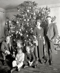 "Dickey Christmas tree, 1922." Our fourth holiday visit with the family of Washington lawyer Raymond Dickey, who has a decade's worth of Christmas portraits in the archives of the National Photo Co. Some of which turned out better than others. View full size.
Dave&#039;s Understatement:"Some of which turned out better than others." Boy, I'll say! It's amazing how many times I find myself hitting"Send To Trash" while editing my own photos. Big plates weren't cheap I don't imagine, so these fellas had to let things slide. Merry Christmas to ALL!!! (but when More (allegedly) wrote "A Visit From St. Nicholas," Santa says "Happy Christmas to all" -- the editors changed it. So, Happy Christmas to ALL of you fine folks too.
The Barbara Walters InterviewBarbara:  "If you were this Chwistmas twee, what would you say?"
Me-Tree:  "Could someone put a little Tylenol in my water - I have the worst crick in my upper trunk."
Are We Having Fun Yet?How exciting to see a comment from Zippy the Pinhead's creator on Shorpy!  
Great Grandson of famous photographerJust bought a print of a William Henry Jackson photo from the Detroit Publishing Company, circa 1900. WHJ was my great-grandfather. I have very few of his actual photos---nice to be able to see and obtain more here!----Bill Griffith (William Henry Jackson Griffith)
Big ContrastThere certainly is an obvious difference between the grim Dickey clan and tterrace's family. 
Oh, MinBack in the 1920s and '30s, "The Gumps" was a popular comic strip, with Andy Gump and his wife, Min.  "Oh, Min!" was a catchphrase back then, so I suppose the album or whatever it is was associated with the strip.
Anything BUT merryThe juxtaposition of the message "Merry Christmas" with the subjects' grim facial expressions is extremely incongruous, and gave me an unexpected laugh.
Happy Holidays, everyone! Truly.
Way back whenBack in the day before fire safety took the fun out of everything, my elementary school had a similar Christmas tree in the front hallway.
Not only was it glorious, it smelled wonderful.
The last year we had one was 1965, the next year the principal set up one of those aluminum monstrosities.
Wonder what became of the ornaments.
Great Shorpy photo as alwaysbut like most commenters, I'm wondering about the unhappy faces.
Two theories:  Either they just found out that the Redskins once again missed the NFL Playoffs or someone recently informed them that the Great Depression was only seven years away.
The Joy of ChristmasLooks like everybody's getting socks and underwear this year.
Nice tree.The faces of the younger woman and the boys almost look like cardboard. It's probably from the flash. What a great picture.
Worn to a FrazzleThat poor Mother looks like she is just completely worn out. The hairstyle reminds me of Elsa Lanchester in "Bride of Frankenstein". The "thousand yard stare" in her eyes makes me sorry for her that Valium had not been invented at that time. Sure hope they all had a better Christmas than their picture projects.
Oh Min!Oh Min! was a song released in 1918, sung by Edward Meeker, based on a catchphrase from the comic strip "The Gumps." Apparently in 1924 there was a motion picture by the same name.
re: Big ContrastYeah, but they definitely have some of our ornaments.
Christmas CheerEggnog and Jack, STAT.
Bah! Humbug!It must be true what they say about those black-hearted lawyers!
"Don't be sad, kiddies; tomorrow we can go back to our usual Dickey lawyering!"
Aside from that, it is nice to see all those wonderful ornaments I remember from my childhood. 
Could they look any more miserable?Man this is a somber looking bunch, the only one with any real expression is the kid in the Sailor Suit.
Love the tree! Real glass ornaments with elaborate decorations, not the cheap plastic or plain glass junk you find now.
Another Christmas photo from the same eraHere's a photo from about Christmas 1922 taken by my grandfather Wilford Fletcher.  On the right is my mom, Margaret, and on the left is her older sister Dorothy.
Oh Min!What is it?
[Looks like a game or a phonograph album. "Oh Min!" pops up periodically on eBay.  - Dave]
Mry Xms -Hpy NwYrI would like to wish for each and all the Shorpyites: "Best of the Season!"
  To Dave especially - what a monumental amount of work this is - I don't think folks can really appreciate that until they've tried to do a bit of itinerant webmastering...    I can just see the typical Louis Wickes Hines photo of Dave, standing in front of his computers: 
"David, looks 65, says he is much younger, been a webmaster for several years now, makes very little for his efforts. Works 15 hours a day, gets no exercise and little sunlight or fresh air. Hands are always sore from typing and processing digital photos. Eyesight suffering. Perhaps no hope for David to have a 'normal' life."
Thanks to tterrace for his contributed (and ongoing) "stream of richness" and for drawing back the curtains over a window into the fascinating 3-D web of lives of his family and friends.
Thanks to all the Shorpy contributors, from the 'Anonymous' one-line drive-by snarkings, to the Rest of the Bunch.
  May each of us find some quiet and contentment in the midst of busy lives and times!
  So: Murray Ecksmiss and Hoppy NuYeer, etc etc!
Cheers
Zephyr
&quot;Merry Christmas From the Family&quot;I hope at least a few people (besides me) got the reference made in the title of this post to Robert Earl Keen's very funny song.
Tall TreeThe tree looks like one of those shown in a past picture..
A 12 foot tree in a 10 foot room.
(The Gallery, Christmas, D.C., Kids, Natl Photo, The Dickeys)
