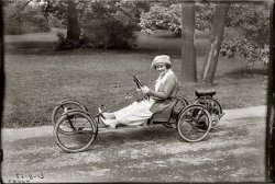 New York, 1920. Ms. Young returns, piloting a less imposing conveyance but still with a gleam in her eye. 5x7 glass negative, G.G. Bain Collection. View full size.
The Smith FlyerA company called A.O. Smith originally had the rights to these motors and along with Briggs manufactured the Smith Flyer. They were not very successful because of the lack of power. But B &amp; S went on to become the small motor supplier for a multitude of uses.
Whatizit?It's a Smith Flyer.
[Close. Briggs &amp; Stratton Motor Wheel. - Dave]

Fifth WheelMs. Young isn't exactly dressed for tinkering with a finicky one-lunger.  Nonetheless she and her outfit are spotlessly clean.  Her pit crew must be nearby.  Wait'll her father finds out about the bad trade she made.
Nice go cartLooks like it might have blown some air somewhere unladylike, though....
You've just got to enjoy that fifth wheel for power.
Smith Motor WheelA.O. Smith purchased rights to manufacture the British-designed Wall Auto Wheel. They made a number of improvements to the original. Briggs &amp; Stratton continued to improve it after their acquisition. A surprisingly large number have survived.
Red BugThis vehicle is known as the Briggs and Stratton Flyer. They were also called "Red Bugs" because they were painted red. I own an A.O. Smith Motor Wheel (just the engine). The engine, both the A.O. Smith and the Briggs and Stratton were sold seperately to be attached to bicycles. Most of the engines were sold for bicycles, and only a few for the Flyer.
(The Gallery, Cars, Trucks, Buses, G.G. Bain, NYC)