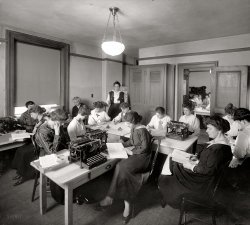 Washington, D.C., circa 1920. "Office with women and typewriters" is all it says here. National Photo Company Collection glass negative. View full size.
Studying the manualThey are all trying to figure out how these things work. "Now where's the ON switch?"

Working conditionsThere is not much desk space for them -- they make the modern cubicle look like a spacious office in comparison. Note the additional bunch stuffed into the next room as well. 
It must be stifling to have that many people working in the same room on hot summer days in Washington DC, before the days of air conditioning. No ceiling fan for these ladies, either.
And based on the relative lack of clutter, I expect that they remove all their belongings at the end of the day, rather than keep papers around till next time.
This has been a testIf it were real, you would all have your own desk.
It looks like some sort of pre-employment exam, testing the candidates for reading speed, comprehension and speling.
The lady in a chair in the foreground and the other in back with the whip in her left hand pretty much precludes an every-day-is-like-this situation. 
Who left the tuna sandwich  in the icebox overnight?Yes, it is an office.
Yes, there are typewriters.
Yes, the people in the office are women.
But I am not convinced that this is where they sit when they do their work each day. This appears to be some kind of meeting or gathering taking place.
Notice that the women to the right have no desks and there is really only one typewriter per table. (One typewriter has been moved to sit at the front table, with another already there, so the women with the inkwells and pens have a place to write).
What this company did, might suggest what kind of meeting this was. But it seems clear to me that this is not how this room looked when these women were doing their daily tasks.
[This might be the District Building on Pennsylvania Avenue. Room 509 is where bids submitted for various municipal contracts were unsealed. Anyone there on the fifth floor today, send us a pic! - Dave]
I didn&#039;t realize that women wore spatsHowever, the woman in the foreground is wearing them.
I always identified them as a form of wear exclusively reserved for men.
The last time I saw them worn was back in the early 1960's.
I was passing by an old investment house in the financial district of a large city.
A chauffeured Rolls-Royce came around the corner and picked up an elegantly dressed older gent.
I noticed that he was wearing spats; what a grand old guy!
(The Gallery, D.C., Natl Photo, The Office)