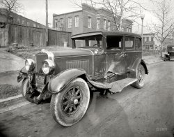 Washington, D.C., 1931. "Auto accident." I will leave it up to Shorpy Nation to determine the location and make of this dented dreadnought. 8x10 safety negative, National Photo Company Collection. View full size.
What exactly is that lightmounted slightly in front of the drivers door, almost on top of the hood? An extra headlamp? A searchlight? I ask because my father once owned a decrepit 40 Ford model sedan that had exactly the same thing, but it was so long ago (I was just 6 or 7 years old then) I never found out what it was for before he sold the car for scrap.
[Parking light. One on each side. - Dave]
MeowThere appears to be a kitten coming through the hole in the gate at the very precise moment the photographer took this picture, thus memorializing himself for eternity or for at least as long as the picture lasts.  Very clever, these felines.  (Or is that a piece of debris?)  
Not that badIt'll buff right out!
Good ObservationIf that ain't a cat it's a dog.
I also like the stone curbs.  There are areas in the city I live in that still have stone curbs and brick streets.  
This boat hit everything!Front bumper torn off.
Base of radiator pushed back.
RF Fender crumpled
Right headlight turned a little outward.
LF Fender crumpled.
Running board bent downward.
Drivers door is crumpled, with a section rolled up into a fist sized ball.
LR Fender bent.
I'd venture to say this guy did all this himself going to fast, spinning out, and bouncing from solid object to solid object.
[Also: Large hole in windshield on passenger side. - Dave]
The Shadow KnowsAlso memorialized are the photographer's and his camera's shadows!
Danger glassI didn't even notice the broken windshield. What can be seen is a clean break, as the large shards are absent in this view. I would have been looking for the telltale spiderweb of modern laminated safety glass, an invention that is too easy to take for granted.
Based on the hubcap design My guess is that it's a Peerless.
[You were the only person to venture a guess, and you are correct! Circa 1930 Peerless. - Dave]
Buff right out?At least this was in the days when it *could* be economically repaired! Other than the panel in front of the driver's door (which probably could be buffed out), everything else damaged just bolted on.
Today, if that car were more than a few years old, it'd be totaled by the "insurance" company!
ScenarioHit in the driver's side door by another vehicle, which propelled it off the road causing the front-end damage.  Doesn't explain the left rear fender well, though.
Such a masculine machine -- like a boxer cut and bruised after a fight.
Glass Cabinet CarsI'm told that for years, my Dutch immigrant grandparents refused to ride in a "glazen kast" (glass cabinet) car because of the danger of glass shards as so clearly evidenced here. Maybe they had a point back then!
Double JeopardyYour grandparents were right. The glass in these cars were extremely dangerous. Equally dangerous were the steering columns which were not designed to collapse during frontal impacts. It was not uncommon for a drivers to be fatally impaled from frontal collisions at speeds as low as 25 mph. So much for the saying "they don't build 'em like they used to"! 
A PossibilityThe only crash I can come up with which might match this is the June 1931 crash of the wife of Pennsylvania Senator Davis in Frederick, Maryland, as she was on her way back to Washington from Gettysburg PA. She was driving a coupe and struck in the side while passing a milk truck. No serious injuries, but it did warrant a trip to the hospital.
[This is a four-door sedan, not a coupe. - Dave]
Those Galvanized TubsThose tubs had a great many uses outside their primary use of scrubbing board washtubs.
I spent many a summer day in one as it did duty as an outdoor pool and come Saturday night you could fill it with a 25 lb slab of ice from the ice man to cool down the Royal Crowns and Gunther beer for a backyard party.
Also with a broomstick and twine it doubled as a bass fiddle or if you liked Krupa or Cole you could bang away with a couple of sticks to the tune of either Topsy or Turvy.
1929 PeerlessAppears to be a 1929 Peerless. 
(The Gallery, Cars, Trucks, Buses, D.C., Natl Photo)