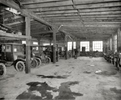 January 1925. Fairfax County, Virginia. "Makely Motor Co., Falls Church." Our second look at this establishment shows a number of Model T Fords in the service garage. National Photo Company Collection glass negative. View full size.
Eat my dust!I hope repairs include a complimentary car wash.
Oil SpillFrom the looks of the floor you would think sawdust and push brooms  hadn't been invented yet. And, while I'm at it: From the looks of the car lineup I'd guess the turnaround time for a ring and valve job would be three years.
My GrandfatherCalled them "T-Model" Fords.  I wonder how common that usage was.
He often spoke fondly of a trip he and a buddy took across the country to the Grand Canyon in one.
DeflationThe two in front appear to have been sitting there for a while, the tires have lost about half their air.  Or, did they sometimes run them that low?
Time MachineWhat a great picture! Shorpy really is a time machine! It's like you just strolled into this shop to see what was happening. Those tailpipes stored in the rafters look for all the world like a set of headers for a fuel dragster.
How many cars do you see there? I count eight plus what looks like the windshield and steering wheel of a ninth through the windshield of the fourth one from the left. And what the heck is that in front of the fourth car?
[I see eight cars, including the steering wheel in back. "What the heck" looks like an upended coupe body. - Dave]
The floorlooks like the St. Valentines Day Massacre was last week.
Early hardtopThe coupe in the front low on air is a rare sort -- Ford made coupes with a removable pillar in  1918 only, with the pillar stored in a compartment behind the seat. You could lower the windshields all the way back. Few were sold and very few survive. The upended body is a 1923-25 roadster, probably brand new. Ford sold new roadster bodies for $60 in 1923, with upholstery but without a top or windshield.
(The Gallery, Cars, Trucks, Buses, Natl Photo)