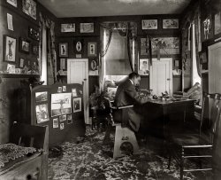 "H.E.F. in den, 2227 Nichols Avenue," circa 1920. Herbert E. French owned National Photo, the source for so many of the images seen here. Evidently he surrounded himself with his work. National Photo glass negative. View full size.
Sense of HumorH.E.F. seems to have a great sense of humor with his walls covered in "posters" and beautiful women... he even has a prank-type of toy... seems like a modern day frat boy almost.
Yet another placardYou should be ve-ry careful, you know,
you might get interested
in your work, and
let your pipe go out.
-- James McNeill Whistler
I am waitingI can only hope someone can explain what the fascinating object in the photo on the board might be.

Poster OptimismNote the poster to the left of the door:
"CHEER UP THERE AIN'T NO HELL"
Humm, interesting!
Hef!Most photos titled "Hef in Den" would have a rather different assortment of pinups on the wall.
Show Your ColorsHerbert apparently liked this poster but wasn't so keen on the advertiser.

source: Library of Congress
The previously noted "Cheer up there ain't no hell", was copyrighted and printed by the Celebrity Art Co. of Boston Mass.
I love the bulldog print too; it looks very modern.  I know its a stretch, but something about the expression reminds me of George Rodrique's Blue Dog series
H.E.F. styleH.E.F. was an Arts &amp; Crafts kinda guy, wasn't he?
Psst! Look behind the man&#039;s seatI think there's a snake on the floor. But is it real or is it a model?
EEK!I just saw the large snake (boa?) on the rug behind Mr. French.  Wonder if it is alive.
[It's a wood snake. - Dave]
Thar she blows!The fascinating object appears to be a harpoon gun without a mounted projectile and rope. I'm fascinated with the Gibson prints hung overhead.
Lair of the black mambaOn the rug, slightly to the left of his chair.....is that a rubber snake?
No more waiting.The "fascinating object" might be a naval deck gun, dating from the turn of the century on.
Mixed molding messageH.E. is using his chair rail as a picture rail...
HEF&#039;s decorI think some of this constitutes examples of his work. National Photo shot ad layouts -- composites of artwork and type for brochures and flyers. A lot of the printing seems to have been done by Standard Engraving. Together they did postcards, novelties and souvenirs for the National Remembrance Shops. At least this is what I gather from some of the National Photo commercial stuff that I've come across the past couple of years.
Who&#039;s there?Above the door on the right:
Opportunity knocks daily
Usually in the morning
My, My, My...all those saucy ladies on the walls.
A kindred spirit. . . with a love of photography and boxers. (The canine variety)
ReflectionThe matted photo to the upper right of the gun photo looks to be the Washington Monument and reflecting pool.  Yes?
PipedHe's a fan of tobacco. Could be a water pipe on the desk. 
OfficeBy the looks of the top hinge on the door on the right, it seems to have been opened quite a bit.  I'd suggest it is a door to the outside.
Old PrintsI think I have a few of those prints high on the upper right wall. They're printed on thick stock and one says "Copyright 1903 Collier's Weekly."

Roycroft and GibsonH.E.F. was very fond of Charles Dana Gibson. The curious chair looks very much like Roycroft work, and there are what appear to be several Roycroft printed mottoes pinned on the wall, though I am not sure if "Cheer Up, there Ain't No Hell" is one of them. 
What is it?What is the purpose of that object setting on the left side of his desk that looks like a tangled hose? Is it a work of art?
[Looks like a speaking tube. - Dave]
BlamMethinks the weapon is what was called a naval quick firing gun.
PressedIf those were three ironing board cupboards, that would explain "There ain't no Hell." Who needs hell when you have ironing?
Slithery message to the maidWith a few changes, I could work very happily in this room.
1. Add a computer.
2. Throw out the masochistic desk chair and bring in something with a bit of pad and swivel.
3. Exchange the wood snake for a cat and a note to the maid, "Leave this room alone."
Seriously, what is the deal with the snake? Highly irregular, I'd say.
No snakeI thought it was a snake too, hubby said no, it's a cane.  I guess that would make more sense.
[Hubby is wrong. - Dave]

The Little DoorsI wonder if the little doors are for those built-in ironing boards we see so often in Warner Bros. cartoons. They're on an exterior wall so unlikely to be cupboards.
[Three ironing boards? - Dave]
The mystery objectappears very similar to a mariner's or astronomer's sextant, but not exactly.  Whoever comes up with the correct answer should win two autographed 8 x 10 glossies of Keefe Brasselle.
What funI spent a very long time just enjoying this room. Thank you.
ClosetsThe closet doors in my house (built in 1926) have the same latches. 
(The Gallery, D.C., Natl Photo, The Office)