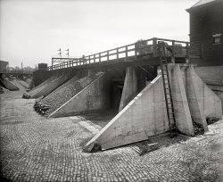 Another view from 1925 of the W.H. Hessick &amp; Son coal yard in Northeast Washington, D.C. By December 1925, the company had moved to 14th and Water Streets S.W. National Photo Company Collection glass negative. View full size.
W.H. Hessick coal yardDave, I think these photos of are of the Hessick Coal yard at 14th and Water streets S.W. Three reasons:

If these photos were of of facilities at 53-59 N sreet N.E., why would the sign have to include the information regarding the location of the office?
  Consulting the 1919-1921 Baist Realty Maps, the orientation of the pictured sidings corresponds very well with a coal yard at 14th and Water streets S.W. (shown below).  The maps of the area at 53-59 N sreet N.E, while close to the B&amp;O tracks, shows no coal yard or similar sidings.  In addition to the general track layouts, two additional details seem to fit with this location:  The Bradley School was located at 13 &frac12; &amp; D streets S.W. and could be the building visible in the background (under the gantry crane) of the earlier photo;  The signal bridge shown in this photo is consistent with a location over the main tracks of the Philadelphia, Baltimore and Washington Railroad 
.
 A 1924 advertisement (also shown below) displays a line of trucks in front of what appears to be the facilities at 53-59 N St N.E.  It is not the clearest image but the buildings and signage appear quite different from these photos.


(click on images for larger versions)





[The company's advertising prior to December 1925 has the coal yards on N Street N.E. The map below, from 1919, shows numerous coal yards and sidings there. The yard would have the address sign because it's east of the main office. Click to expand. - Dave]

(The Gallery, D.C., Natl Photo, Railroads)