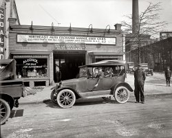 Washington, D.C., circa 1925. "Northeast Auto Exchange, H Street." My favorite kind of National Photo photo, something that might be called unintentional-slice-of-life. National Photo Company Collection glass negative. View full size.
One for the road"Alcohol for Automobiles" -- I'm assuming it's engine-related, and not driver-related!
Well, I triedAll I get at "www.d.c.comm" is "server not found." Shucks.
MethanolMethanol, or as they also called it wood alcohol or methyl alcohol, was used as an antifreeze to keep the engine coolant from cracking the block in cold weather.
[A potent poison as well. - Dave]
Morris HersonI wonder if that is M. Herson in the coveralls. According to the census, Morris Herson was born in Russia and immigrated to the States in 1895.  



Washington Post, Jun 4, 1929


Morris Herson, 44, is Dead.

Morris Herson, 44 years old, an automobile dealer, died at his residence at 514 F street northeast. He is survived by the widow and three children.

ContinuitySee the name M. Herson in the window? Now Herson's Honda in Rockville, Maryland.
And Now ...The 'hood had a smidge more charm back in the day. If it still existed, 62 H Street NE would be somewhere under this overpass near Union Station.
View Larger Map
Coulda used these guys a couple years agoThe shift linkage of my car broke in the parking garage beneath the office building that now stands where this garage once was.
On second thought, they probably didn't carry any VW parts anyway.
LaterThe Hersons owned Manhattan Auto in Bethesda, where in the 1950s, you could go and ogle the spiffy Jaguars, Porsches, and various other future classics then go across the street to Giffords for a really classic banana split!  That's why they're called "the good old days"!
Turning left.When I was a kid, in the 60's before turn signals were common on motorcycles, we all signaled our left turns with a gesture identical to this fellow's.
Alcohol for AutomobilesMethanol (wood alcohol) was used as an antifreeze for the car cooling system, but it gradually boiled off and had to be replaced. There were testing devices, similar to the bulb-type battery testers, that could be used to tell when the alcohol needed to be topped off in your radiator in order to remain effective. 
Eventually wood alcohol was replaced by "permanent" antifreeze, usually made with ethylene glycol. This is normally dyed fluorescent green, and is what comes to mind when we think of the term "antifreeze" today. Both types of antifreeze are poisonous.
As a big bonus, the ethylene glycol based antifreeze also facilitates the cooling function of the radiator. Those of us over a certain age will remember car radiators "boiling over" when driving in hot weather or climbing mountains. Those days are long gone, thanks in part to modern antifreeze/coolant!
To remember which alcohol is the drinkable kind[A potent poison as well. - Dave]
To remember which alcohol is the drinkable kind: "Ethyl can't drink methyl."
Hersons of InterestSurprisingly, at least to me, the later Manhattan Auto Inc.  and still-existing dealerships, were formed by a completely different Herson family: three Lithuanian brothers who emigrated circa 1914. Robert Herson (1892-1975), founder of Herson Auto Parts &amp; Glass. David L. Herson (1896-1959), president and owner of Manhattan Auto Inc.  Nathan Herson (1906-1971), president of Herson's Auto stores in Washington and Rockville.
The Herson familyMorris was my uncle.  David Herson was my father.  Morris' sons were Mitchell, who became a dealer for Kaiser Frazer, and Abe, who worked with my father and later me at Manhattan Imported Cars.  Abe was head of Jaguar service in the sixties and later was a Jaguar salesperson at Manhattan in Rockville.
Nathan Herson, another uncle, was the Herson of Herson's Honda, not Morris.  Nathan's son Gerald is the current CEO of Herson's Honda and Mitsubishi, both in Rockville.
ResultsIsn't it interesting how my memory of Manhatten Auto could bring such results.  All appreciated; good memories of Manhatten Auto on Wisconsin Avenue and of Mr. Mann who worked there. Thanks to J. Herson, as well.
This is one of the joys of Shorpy; a comment can be expanded  or corrected by others.  So it is often a valuable learning experience. 
[Today's lesson: There's no "e" in "Manhattan." - Dave]
A strong personIs Morris Herson, if that is indeed him in the coveralls.  He looks like he could have bench pressed that car in his prime.
Five decades laterHere's a sidelong view of that building (looking almost due east along H St.) in the late 1950s. In 1974, it would be demolished for construction of the overpass rerouting traffic over the Union Station tracks.
(The Gallery, Cars, Trucks, Buses, D.C., Natl Photo)