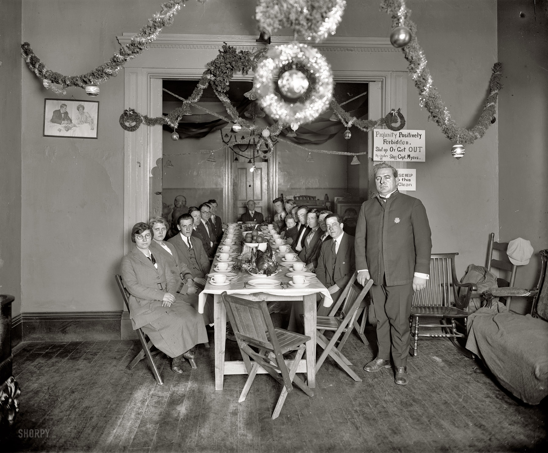 "Volunteers of America, Christmas 1925." A festive table, good friends and that venerable yuletide sentiment "Profanity Positively Forbidden -- Shut Up or Get OUT." Merry Christmas! National Photo Co. glass negative. View full size.