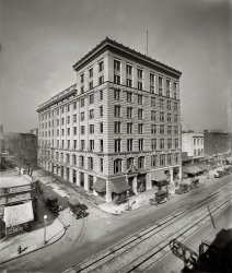Washington, D.C., circa 1923. "Victor Building, Ninth Street N.W." National Photo Company Collection glass negative, Library of Congress. View full size.
Victor BuildingBuilt in 1909, with an addition around 1912 that more than doubled the size. You can see distinctions in the facade: the left half is the older bit. The shell of this building still stands, it recently underwent extensive renovations resulting in a modified outward appearance.
Access Hatches?Anybody know about those things that appear every 10' or so along the tracks? I'd guess they're metal access doors with an anti-skid type surface. What was under them? Why so many? Why the pairing of a big one and a little one? I assume that's a cable car track, and if that's true, then maybe those are where the cables guides were located and needed to be cleaned and greased? Can I ask any more questions in one post?
[These are electric streetcar tracks with the power supply in the slot between the rails. - Dave]
(The Gallery, D.C., Natl Photo)