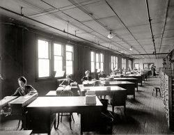 Washington, D.C., circa 1926. "Internal Revenue." A seasonal reminder from Shorpy. National Photo Company Collection glass negative. View full size.
DrabAll the office pictures Dave has shown from this time period seem to be so drab and lifeless.  The one thing I notice is that all the desks are angled to take advantage of the window light.
One Laptop PC EquivalentI could imagine the clerical work being done by this group expressed in increments of "laptop power."  This would be analogous to "horsepower" as a unit of physical work.  One laptop should do everything you see here:  the data collection, storage, calculation, and reporting.  For better or worse, it would displace all these people and their filing cabinets.  And it would save the floor from getting even more beat up from the foot traffic.  
Ditto, ditto, dittoSame desks, same windows, same mini file cabinet on the desk. Same full tray of work for each of them. Same add-on electric cords, hanging from the ceiling.
Almost the same hair. Almost the same smocks on every woman.
These jobs make the prospect of stringing beans in a canning factory with 40 barefoot children look liberating.
This would seem to beThe Franz Kafka Annex. And yes, we do have your files. So glad you asked.
AuditAs they select the poor souls who are about to get audited here's hoping I am not one of them.
SymptomsTwo desk are empty. Stacks of work waiting. Both employees are rumored to be recovering from boredomitis. This malady has plagued the department's workers for some time. No known cure. 
Symmetry Undoubtably, the atmosphere wasn't the best for preventing boredom, but I find it artistically pleasing to the eye. It's a nice picture even if it wasn't a nice job. Though I personally think it could have been the latter, too.
Looks Preferable to Me!I look at that old industrial mill-type building and actually wish I worked there rather than in these cubicles they've got us in here at my insurance company.  The great minds here have us in a beautiful color scheme of beige on beige with beige accents.  Anyone else hate cubes?  When I first started in this industry we had an open floor plan with desks lined up like those but in a newer, cleaner office building.  Each desk had a phone and an in/out bin.  No computers at all.  It was better and more comfortable back then, I think.
Clerical workI was a file clerk in the early 1970's and a lot of this scene is reminiscent of that job. We had bundles of things to file, in my case, traffic tickets or driver's license applications, all roughly the same size. we had the cabinets to file into.
To stave off boredom sometimes we had impromptu filing competitions, who got done with a bundle first won.
ShipshapeI can't help but notice how clean and organized everything looks.
I wonder alsoWhat are those drop cords connected to -- some kind of punching or imprinting doodad? 
Peaceful by contrastThe photo of everyone lined up at the IRS office looked a bit chaotic and disorganized. When you put all that paperwork in the right hands, it becomes nice and tidy.
If this were a normal enterprise, like a hardware store for instance, I'd much rather be out on the front lines working with the hordes of customers than keeping the paperwork neat. In the case of the IRS, though, I suspect every single one of those people out at the front counter is a dissatisfied customer. This would be one of those times when I'd opt for one of these quiet desk jobs.
Mystery powered box on deskThe drop cords on the left power something on the desk.  It's that oblong box under the clerk's left hand.  I wonder what it is.
(The Gallery, D.C., Natl Photo, The Office)