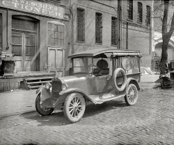 1926. "Semmes Motor Co. truck, Walter Brown &amp; Sons." Another from National Photo's series of Washington, D.C., working trucks. This Dodge's battered body notwithstanding, motor trucks were a relative newcomer to a workaday world where dray wagons and horse teams had long dominated. View full size.
Adam Weschler AuctioneerIt's nice to see the truck in front of Weschler's Auction House (warehouse?) now at 909 E Street NW.
http://www.weschlers.com/ 
Lord Baltimore&#039;s White ArchAnyone have any idea about the arch on the right, what's written above it, and what's in the space--fire fighting apparatus of some sort?
[It's a Lord Baltimore filling station. The thing sticking up is the glass globe atop an "American Strate" gas pump. - Dave]
Dave, thanks for answering this.  -lesle
Butcher BrownWalter Brown was a butcher at Center Market. The location is the north side of C Street NW, now the National Archives.  We see here the rear of buildings which faced on to Pennsylvania Avenue. Adam A. Weschler Auction House was at 920 Pennsylvania Avenue. Lord Baltimore Filling Station  No. 1 was at 912 Pennsylvania Avenue.
The Shorpy post, Street View: 1922, shows an aerial of the larger area.  The burned-out furniture store at 910-912 Pennsylvania Avenue would become the Lord Baltimore Filling Station.
In contrastit looks like a brand new, shiny 1926 Model T Ford behind the beat up old Dodge.
Weschler FireThis spectacular three alarm fire was reported in the Washington Post 26 March 1915 on page 5. I have a copy of the WaPo article if anyone is interested.
I am so grateful for a photo of this fire damage! My great great grandfather's hotel and saloon, Bessler's Hotel, was next door at 922 Pennsylvania Ave. NW. Bessler's hotel and saloon was also extensively damaged due to the fire and had to be completely evacuated. 
The fire may have been linked to a growing dislike of the hyphenated Americans as tensions mounted pre World War I. Bessler's Hotel had a hall where many German-American citizens gathered and on 26 Aug 1914 one of these groups declared themselves loyal to the fatherland (Germany). That must have caused some strong feelings, IMHO.
(The Gallery, Cars, Trucks, Buses, D.C., Natl Photo)