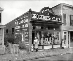 Washington, D.C., circa 1925. "F.G. Lindsay store front, Anacostia, 2215 Nichols Avenue." Exterior of the grocery seen here. National Photo Co. View full size.
And Meats!Nothing like a side of beef hanging in the front window to get your appetite going!
Proud craftsmenNotice how the sign company branded the wall sign? Even the overhead sign was signed!
Ever see a vinyl letter job in some store window get autographed?
Now THAT iswhat I call a meat market ! And they also sell popcorn.
Paging Lewis HineChild labor gone completely M-A-D!
HmmmThe tot looks like the Uneeda kid.
The street name was changedThe street name was changed to Martin Luther King Jr Avenue. I believe it stood where the parking lot is now as the street numbers are even on the other side.
&quot;Buy this Flour&quot;Oh yeah! and what if I don't? 
I&#039;m so oldI remember when Nichols Avenue was Nichols Avenue.
Lindsay RoadI grew up off Lindsay Road Oxon Hill, not far from Anacostia.  wonder if this is man (or child) is related to its namesake?
SeparatedI didn't notice the boy on the right at first. He looks sad and lonely.
I know, I knowHe's a butcher, I get it, but I would probably be ill buying fresh meat from this man with the hunk of meat just hanging around in his window and the filthy apron.  Guess I'll stick to Cub Stores and get the meat refrigerated.  Yes, I am a spoiled woman of my time.
I am not going to say this again"Mister, I will be back here tomorrow morning bright and early and I had better be seeing some flypaper hanging near that beef! The Board of Health is just not going to cut you any more slack. Oh, and from now on turn your apron inside out every day around noon.  Say, wrap me up a couple of those pork chops, OK?"
(The Gallery, D.C., Natl Photo, Stores & Markets)