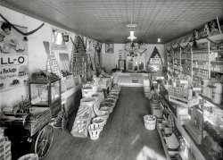 Washington, D.C., circa 1925. "F.G. Lindsay store." With some nice Jell-O promotions scattered about. National Photo glass negative. View full size.
Well stockedLots to look at here, from meat to washboards. And this POS display too.
Familiar brandsAnd they are still around today. I could find several Nabisco products, Diamond Crystal Salt, Lava, Sunmaid Raisins, Kellogs on the top right,  Quaker products, Heinz.
For all your popcorn machine needsC. Cretors &amp; Company is still in business
3243 N California Ave, Chicago
www.Cretors.com
Clown-powered Popcorn CartsThe things you learn on Shorpy!
I always thought those popcorn carts with the laboring clown were invented by Disney as gizmos for his theme parks. Oh well. The model in the picture dates from 1909 and if you'd like to see it in color, you can find a photo here:
http://www.oldtoyz1.com/steamengines.html
B &amp; B supplySix years earlier, this must be the place the Junior Marines got their basket and brooms.
I wonderwhat time of year this was taken. Christmas decorations are up, but the windows are open. Either it was a balmy day for D.C. or that place had a heck of a heater, I'm thinking. 
I spyArgo corn starch as well. It's still around today.
Debit or creditI'd like to pick up a few things, but I'm a little light on cash today. Maybe you can point me toward your ATM?
Always facing frontWhen I was a teenager I worked in some of my brother's grocery stores for a few summers. In a well marketed store you will always find the canned goods "faced," meaning every label must be facing forward. This store was immaculately kept and displayed. What a beauty. Back in those days there was only one way to run a mercantile -- the right way.
My great-grandfather owned the first mercantile in Wallowa, Oregon, many years ago in what is still a Wild West sort of rural community of cattle ranchers and Indians. The old mercantile (still open) was my first stop on fishing and hunting trips in the '70s.
It's amazing to walk into such a small store and see it filled with so many items. You can buy anything you could possibly need from groceries to farm feed, cowboy boots, saddles and tack, cast iron skillets, pot bellied stoves, fishing supplies, flannel coats, yarn, bolts of cloth. Sitting on the old wooden front porch sipping on a soda and remembering great-grandpa. Life was good.
MiscellanyThat is the most mysterious bucket of whatever I've ever seen. And it's the most out of place pile of ? right in the middle of a most tidy store.
To me it looks like it could be scraps of wax and or tallow.
However, there also looks to be a handle from a cabinet or drawer mixed in, as well as a door knob. bones, scraps of meat and paper.
Looks like a pail of garbage that someone forgot to throw out.
D.C. WeatherThere's a reason for the expression "If you don't like the weather in D.C., just wait a minute." It can be 25 and snowing on December 10th and 78 and muggy on the 11th. So it wouldn't be unusual to see windows open at Christmastime.
Bucket o&#039; ???Any idea what that bucket might be full of?
Re: Bucket o&#039; ???Perhaps a variety of natural sea sponges.
#3 Bucket o&#039; ???Looks like assorted hard candies.  Wouldn't be Christmas without them.
&quot;Tokio&quot;Containers near the back on the right -- "TOKIO."  Any clues as to what's in them?
[Toilet paper. - Dave]
Tokio mystery containersTokio is an old fashioned spelling of Tokyo.  I expanded the photo as much as possible and the angled writing on the right hand side seems to say "Grade A".  The word at the bottom appears to be "Flour."
My guess is: Tokio Grade A Flour, although I had to laugh at Dave's suggestion that it was toilet paper.  No one is that full of .... oh well, never mind.
[No mystery. The wrappers say TOKIO TOILET TISSUE. - Dave]
(The Gallery, D.C., Natl Photo, Stores & Markets)