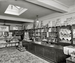 Washington circa 1924. "Cathedral Mansions Grocery." The market at Cathedral Mansions, a multistory apartment complex on Connecticut Avenue that also had its own bakery and drugstore. View full size. National Photo glass negative.
Sawdust on floorsAbsorbed spills. Generally it was swept up each day and replaced with fresh. Very common in shops &amp; bars of the period.
Butter and Egg MoneyButter at 47 cents a pound is equivalent to more than $5.60 a pound in 2008 dollars so we are doing OK on that front.
Even better, if that big can of Criso is four pounds at $1.40, that's equivalent to almost $17 today.  In fact, a 4 pound can of Crisco today costs less than $6.
Good old days indeed!
CocoaThey seem to stock at least six different kinds of cocoa.
Campbell&#039;sCampbell's Soup and Wrigley's Gum have not changed much if at all (except the price obviously). I wonder if the A&amp;P tearsheet behind the register is for comparison purposes or was this store part of that chain? 
Dusting it upSawdust caught a lot of the detritus that fell to the floor, and made it easier to sweep up at the end of the day.
Whoa, look at those melons.Whoa, look at those melons.  Also, I see Kellogg's was pushing bran even back then.
SawdustWhat is the reason for all the sawdust on the floor? At least I hope it is sawdust.
SawdustIf I recall, it was on the floor to make cleanup at the end of the business day easier. The streets weren't exactly clean in those days. The sawdust would absorb whatever was tracked in and at closing, you'd just sweep up and throw away what got dirty and then lay down some more.
SawdustSawdust was used to absorb dirt, mud and grease. At the end of the day, the old sawdust would be swept up and new sawdust laid down. It was also used in bars for a very long time. Eventually, concerns about flammability from dropped cigarettes and improved flooring made it obsolete. Some Creole families and merchants in New Orleans used brick dust for the same reasons.
SawdustThey would put sawdust on the floor because it would absorb the liquids that would fall, making for a easy clean up at the end of the day.
Sawdust reduxMy down-South 60s school custodians used sawdust to sweep the floors. They had big bins of it stored outside the building and I recall us looking in them from time to time. The sawdust seemed wet because it was oily and the combination of sawdust and oil smelled great.
Think about it - faster than wet mopping, absorbed moisture, soft on flooring, and most of all no dust scattered from dry sweeping method (it picked up fine dust and dirt before it can hit the air and settle back). Ideal. I'd order a bin today to tackle our wood floors, pet hair, and teen boys residual in the house.
Sawdust.2Sawdust has long been used on floors to pick up spills. At the end of the day you sweep it out and throw some clean sawdust on the floor for the next day. Ever been in an old-time bar with sawdust on the floor?
Look at the size of the watermelons!
Cheap corn flakesWow...Kellog's Corn Flakes for 10 cents. Wonder what's under lock and key up in that skylight?
SawdustWikipedia has everything! In the article "Floor cleaning," in the section "Methods of floor cleaning," it says: "Sawdust is used on some floors to absorb any liquids that fall rather than trying to prevent them being spilt. The sawdust is swept up and replaced each day. This was common in the past in pubs and is still used in some butchers and fishmongers." I found this through Google, of course.
Received fresh dailyI believe that in those days before modern packaging it was common for many substances to leak, for example the "choice meats" would tend to bleed thru the paper sacks. 
SawdustIn butcher shops (which this is), it catches drips of blood or fat to prevent the floor from getting slippery, and makes it easier to clean up.
That's a dang big scan! Good idea to get a jump on everybody asking for enlargements of certain products.
A &amp; P Bulk BinsThe bins with lids behind the cash-register counter belie the fact that this is an A &amp; P store. I wonder is service was as slow then as they are near me...possibly the store employee is on a higher floor delivering a brown bag of telephoned-in items for the truly cosmopolitan urbanite.
Hmm.Why is there sawdust on the floor?
Paper or Plastic?No plastic bags back then. Check out how all the bread is wrapped in waxed paper.
Zero Scoops"Now You'll Like Bran!" I see five bran choices, mostly Kellogg's, and none includes raisins. Many wheat and corn options too. Mr. Kellogg must have been proud, as he was still alive at this time.
Where&#039;s waldo (a.k.a. the Sun-Maid girl)?The Sun-maid company has a cute history of the Sun-Maid girl: "In 1915, the brand name SUN-MAID was launched, and within a year, executives of the company discovered a local girl, Lorraine Collett Petersen whose smiling face, red sunbonnet, and tray of fresh grapes would become synonymous with the sun-dried goodness of California raisins."
TemperatureMy grandparents used to cook with Crisco exclusively, just scooping it out by the pound.  I remember when I was little getting it confused with sour cream.  The reality was not pleasant.
I notice the packages of eggs on the counter stored at room temperature.  How long do eggs last unrefrigerated?
[How long do they last warmed up under a hen? - Dave]
Hot MothersAs a youngster, I couldn't help but notice that lots of my friends did indeed have hot mothers but in today's connotation, they would have had great advertising potential with that name.  Also notice the cracker barrel in the right at the end of the meat counter and the jars of (probably) olives, pickles, green tomatoes, pickled pigs feet  and pickled eggs on top of the meat counter.  To the person who asked about fresh eggs kept at room temperature, my grandmother kept hers in a glass bowl at room temp for several days  and none of us ever got sick.    Of course she also left the Thanksgiving turkey on the back porch since it could never fit into the icebox.  (We did not ever need any of the BRAN stuff).
Saw what ?I suspect Dave to have kept all these redundant answers to the intriguing question of the sawdust on purpose, just waiting for someone to ask it again.
CalasOK, I know what hams, strip bacon and fatbacks are, but what the heck are calas? Or are my old eyes failing me?
[Cala is short for California ham. Which is not really a ham but a pork picnic shoulder. Also called a "callie." - Dave]
(The Gallery, D.C., Natl Photo, Stores & Markets)