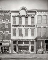 Washington, D.C., circa 1917. "Federal Auto Supply Co., Pennsylvania Avenue." National Photo Company Collection glass negative. View full size.
The legless beggarDid the photographer mean to make a social statement with this picture?  Probably not, considering racial attitudes back then.  But a legless black beggar one door away from a good hot 25-cent meal sure hit me between the eyes.
Dairy LunchI always assumed, when I saw "dairy lunches" mentioned in old novels, that it meant the same thing in gentile circles that it does in Jewish ones -- that is, a restaurant that doesn't serve meat. Looking at this photo, I'm getting the idea that I might have been wrong about that.  Either that or this is the craziest kosher restaurant ever! So what is a dairy lunch, anyway?
[The "dairy lunch room" came to prominence in the late 19th century, offering fast food for white-collar workers. The name signified "not a saloon" as much as it did the contemporary fad for malteds, shakes and ice cream. Dairy bars found new popularity with the rise of the temperance movement and advent of Prohibition. A lot of these places were former taverns. - Dave]
LunchBeen a while since I've had liver and onions for any meal let alone lunch. I'll spring for the small steak for man in need at the drug store. Any idea what the hose near the curb might have been for?
Today&#039;s QueryAnyone know where I can get some hot rolls?
InterchangeabilityHm. Ford Parts next door to Ford Lunch -- maybe I don't wanna know.
Eh?477 would be right about where the Canadian Embassy is now.
A Legless VeteranGiven the dating of the picture as "circa 1917" I think it's reasonable to suppose that the legless man might be a World War I veteran injured in the War.
[He's an old man, so he would not be a WWI vet. - Dave]
The Dairy Lunch todayThe Court Street Dairy Lunch still exists in Salem, Oregon.  A luncheon based on dairy products must have been considered particularly healthsome.
Re: Eh?Unless it was 477 Penn Ave SE, which would put it behind the capital about halfway to Eastern Market. Some surviving buildings in that neighborhood are reminiscent of these buildings.
[This is 477 Pennsylvania Avenue Northwest. - Dave]
Dairy Lunch ReduxOh, of course!  Duh!  Thank you!  To differentiate themselves from the "free lunch" offered by bars, as a respectable eating place.  I suppose the "family lunch" places we've seen advertised in some photos had the same idea.  
Tire TrollopThat appears to be the Kelly Girl in the left door.  An infamous ad from 1910 showed her sitting on a Kelly tire and exposing her ankles!  It was a huge controversy.
(The Gallery, Cars, Trucks, Buses, D.C., Natl Photo)