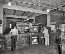The parts department of Semmes Motor Company in Washington circa 1925. National Photo Company Collection glass negative. View full size.
Tell me the truthDo these pants make my butt look big?
[Or could it be the other way around? - Dave]
The guy on the left... missed a belt loop.
Obey that Impulse!At the first drop of rain, put on your Weed Tire Chains! 


Profitable Biz?...cause that looks like the mother of all cash registers.
Getting snubbedGotta love the details in this picture. The Dodge mechanic's run-down heels, the radiator just sitting at the counter, the flower vases next to it on the counter. Then there is the gorgeous display for Snubbers. You gotta wonder what it is even selling. Makes your car drive better when passing playful bulls? Turns out that a snubber is a device used to suppress ("snub") voltage transients in electrical systems, pressure transients in fluid systems, or excess force or rapid movement in mechanical systems. No bull.
Touch of eleganceDon't overlook the bud vases for sale on the right end of the counter. Not something I see at AutoZone these days.
On the right counterIt's the flower vase for a New Beetle. 
Give me your finest frammis...It's for my Nash. And hurry up about it!
Gabriel Snubbers


Bring back the FlowersMy uncle had a 1930s sedan with flower vases that my aunt kept full. They made us feel really special. I can't remember another thing about the car (except that it was black, of course) but that stuck with me.  Better yet, another uncle had a coupe with a rumble seat no kid would forget and which we all fought over.
VasesThe presence of the vases on the right of the counter make me wonder if cars back then had a flower vase option like modern VW Beetles.
SnubbedThe Gabriel Snubber, the first automotive shock absorber, was introduced in 1907.  
http://www.gabriel.com/DisplayTab.aspx?tid=6
In 1900, Claude Foster, a pioneer in the automotive parts industry, founded a company in Cleveland that was named after its first product, the Gabriel carriage horn. Foster later developed the first shock absorbing device, the "Snubber," for which he was granted the first U.S. patent for a direct-acting shock absorber in 1907.

Counter objectWhat are the things the men are examining on the counter? Those don't look like auto parts.
Bud vases!Popular with the ladies. Often hung from the roof pillars or back-seat sail panel inside closed cars.
D&#039;you like my flat?The Tire Mica and Tire Paint are telling of both the poor road conditions and fragile tires of the time. Tire Mica would have been used as an anti-friction agent, both to ease mounting &amp; to prevent chafing between tube and tire.
Highway KnobberyCheck the fancy shift knobs.
Akro Agate Gear Shift KnobsI love the Akro Agate gear shift knobs in the counter case, just in
front of the guy in the striped pants. It is very hard to find an
original one today. You could replace the factory ones, always
black, with a very colorful new knob, they just screwed on and off.
They came in many very beautiful colors, looked like a giant marble.
It was an inexpensive way to fancy up you car or truck. These were
for vehicles with a floor shift transmission. Very Fancy....
re: Counter objectThose machines the clerks are using are early versions of the three-part receipt systems that became common in the 1940s, 50s and on -- until computers took over. As a local printer, we made up and stocked many such forms. Businesses used them widely in our community.
That&#039;s the ticketThose ornate-looking boxes on the counter are receipt machines. Counterman wrote out the ticket, then pushed down on a lever that ejected the receipt and pulled the next one into place. 
WinterfrontThat's not a radiator on the counter. It's a winterfront, an early thermostatic device that was installed over the radiator. The louvers opened and closed depending on engine temperature. They were popular in the colder states.
Some things never change...Even nowadays, some dealers still have under-counter display cases, highlighting everything from oil and air filters to die-cast collectible cars.  Lots of interesting things in this picture, from the cans of Ditzler paint on the shelf, to the display of flashlight bulbs, to the AC spark plugs.  The Gabriel Snubbers appear to be friction-type shock absorbers, using a wind-unwind principle (like a clock's mainspring). The more things change, the more they stay the same.
Sales Receipt MachinesThe customers are watching the clerks write up their sales on sales receipt machines with Art Nouveau style cases. The devices held rolls of multi-copy sales receipt forms, and, when completed, the turn of a handle peeled out one copy for the customer and one or more for the store. Here's two later "streamlined" versions, probably from the 1950s.

DroolworthyThis one scores high on the drool scale for automobilia buffs like me.  I would kill for the Gabriel Snubbers sign.  Lots of goodies here, like the "marble" gearshift knobs in the display case.
Gabriel SnubbersWhat an evocative name! What a gorgeous sign! The contrast in shoe shine on the two customers is marked.  You don't even need to see their outfits to figure out their relative socioeconomic status.  The one on the left has shiny shoes, while Mr. Dodge's are dusty and cracked.
[He's a mechanic. His street shoes could be just as nice as the other guy's. - Dave]
Check out the ChainsWhen I was a kid (in 70's) we had to put chains on our farm truck when we had snow and Ice. I remember they were a pain. Sometimes we would put them on and take them off several times during the winter.
Admiral SemmesThe only Raphael Semmes I'd heard of before reading this was the former US Navy commander who joined the Confederate States Navy and became a famed commerce raider, rising to the rank of Rear Admiral.  Though he called Mobile, Alabama home, Semmes was a Maryland native.  Do I assume correctly the owner of this dealership was one of his descendants?
Heavy liftingNotice the display of jacks on the right end of the counter. These look like a short version of the bumper jacks that were common until the 1980s and the advent of plastic bumper covers used today. The black tubes standing in the center are the jack handles that fit into the ratcheting mechanism of the jack.
A tall mechanic?How do you suppose those greasy hand prints got onto the beam over the counter?
(The Gallery, Cars, Trucks, Buses, D.C., Natl Photo)