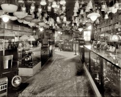 Washington, D.C., circa 1925. "Geo. W. Parezo, interior," 808 Ninth Street NW. National Photo Company Collection glass negative. View full size.
Dim-A-LiteOne of many Google hits for the Dim-A-Lite fixture:
http://www.edisonian.com/p011f001.htm
So, what else do you sell here?Reminds me of when David Letterman visited "Just Bulbs" and "Just Shades."
Lighting Fixtures What a nice selection.  Notice the assortment of "electric torches" (flashlights) in the display case on the left.  I'd like to buy some of these fixtures to put in my home today.
Lamp StoreThere are stores that look like this today, although without the flashlight counter. It must have been a bonanza in 1925 when electric power was firmly situated in major cities. This type of store filled a need for home lighting and probably installed as well as sold these fixtures. The days of a  light bulb hanging from a single wire was coming to an end and properly installed lighting equipment were becoming the norm. The smaller towns came into play as well. The far rural areas really didn't get theirs until the 1930's with government help, like the TVA, and there were probably many areas that didn't get power until well after WWII. The Emerson Radio catalog had "farm radios" as late as the 1950s. A farm radio was an AM set that worked on a storage battery that was charged by a car battery. In the 1970s a couple came into my store looking for such a radio but they weren't available and he settled for a Zenith portable radio that worked on D cells for a fairly long time. The man and his wife lived on a ranch in Wyoming, with no electricity, he looked great in a suit, necktie and cowboy hat, his very plain wife appeared to be a generation older.
(The Gallery, D.C., Natl Photo, Stores & Markets)
