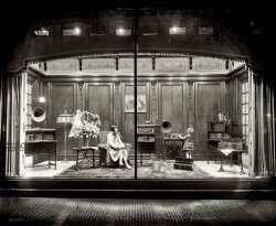 "Thomas R. Shipp Co. Atwater Kent window. Woodward &amp; Lothrop." Department store window display of Atwater Kent radio equipment circa 1926 in Washington, D.C. National Photo Company Collection glass negative. View full size.
Window DressingThat is one "serious" window display, one of the most impressive I have ever seen.  Not very often I say this, but I would actually love to have seen this photo in color.
Modern lifeNote the artwork on the wall -- an older man playing a violin with a young girl at a piano keyboard. A subtle message that society has moved on from "self-entertainment" to a more technical age, perhaps?
Mannequins?So would those be mannequins or live models in the window?
After seeing the manufacture of these radios (1, 2, 3, 4, 5, 6, 7, 8, 9) it is very gratifying to view them in such an elegant display.
 Atwater Kent Radio  is an excellent comprehensive web site with photos, brochures, schematics,  etc...  Most of those pictured here seem to be from the model 40 line.

[Dave, thanks for the close-up.  I'm very impressed with the quality of the mannequins for their time.  The woman does look a bit more porcelain in greater detail. - PER]
Hi-techThe equipment displayed in this window was, in 1926, the ultimate in home entertainment. This was your wide-screen, high-definition, cable-delivered, surround-sound television. Commercial radio broadcasting in North America had only been in existence for just over 5 years and was still a new, exciting and constantly-developing medium. No doubt a lot of time, effort and money when into this dramatic display.
Bruce
Atwater KentsThey are from left to right - Model 30 in a Pooley cabinet with an H horn sitting on top (just for looks as the Pooley has a built-in horn). On the woman's right is another 30 in a different Pooley cabinet. The girl is operating a Model 35 with H horn; on the floor is a Model 30 in a normal cabinet; on the right is a Model 32 in still another type of Pooley cabinet; on the table is another Model 32, this one in the normal cabinet.
(The Gallery, D.C., Natl Photo, Stores & Markets)
