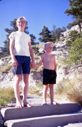 Here we are, my little brother and me, on another family trip. I had my geeky glasses on. I'm sure our parents ordered us to hold hands for the picture. I think we were in Wyoming or Nebraska, summer of 1969, visiting Dad's relatives.
My puberty was kicking in and I was sure anxious about starting 9th grade and facing those showers in PE! View full size.
Puberty and public showersI joined the band in my Dallas junior high (1968) to avoid public showering.
SimilaritiesI had the same kind of glasses and wore the same cutoff shorts! And I can imagine that after my parents forced me to hold hands with me little brudder for a pic, I'd toss him down the steps just to even things up.
60s vs 80sIn my 1981 CA high school band, we changed on the bus (co-ed).
Only jocks showered at school.
re: On Vacation 1969Boy, tell me about it, Mvsman. I don't know about you, but for me PE turned out to be every bit the living hell I'd been dreading. At least I had some degree of ability with track &amp; field type stuff - hill dweller's legs came in handy for running and jumping - but everything else? Forget it. Me to a football: What am I supposed to do with you? Nice shot - somebody in your family knew what they were doing, making sure there was some fill lighting here. As for the geekiness of your glasses, the young twenty-something gal at the Apple Store where I bought my new computer last week had on a pair much like that. I thought she'd gone back in time and swiped a pair of my father's. I thought this could use some color correction, so here's what I came up with.
NebraskaLooks a lot like the Pine Ridge of western Nebraska. My family owns a "ranch" out there (really a hunting cabin). The tree on the upper right appears to be a Ponderosa pine, which grow all over the Pine Ridge. I most likely have a picture of myself at that time, looking just like this.
High schoolGreat picture, even though you may have hated holding hands!  PE was also horrible here.  Not only was I terrible at everything, but the teacher was happy to share with the whole health class how bad I was.  This did not accomplish his aim, which I can only assume was to somehow make me do better via shame.  
Dork matter detectedWe didn't go through Nebraska but I was travelling out west that same summer, in MUCH geekier glasses (pretty much GI BCG-style of the period) and much more gangly. Nobody expected me to hold anyone's hand in pictures though. I made it to puberty before high school but one thing that made running cross country attractive to me (besides being somewhat good at it) was that we got through the showers long before the jocks got there.
Musical AbilitiesAlthough I studied classical piano from about age 6, and branched to pipe organ at 12, I play violin and viola also because three weeks into my HS freshman year (I was 13 in 1966) an opening in the school orchestra came up and I was able to substitute that for goddam PE, and the jocks, and ...
   the SHOWERS!!!
No kid ever learned to play a violin so fast.
(ShorpyBlog, Member Gallery, Kids)