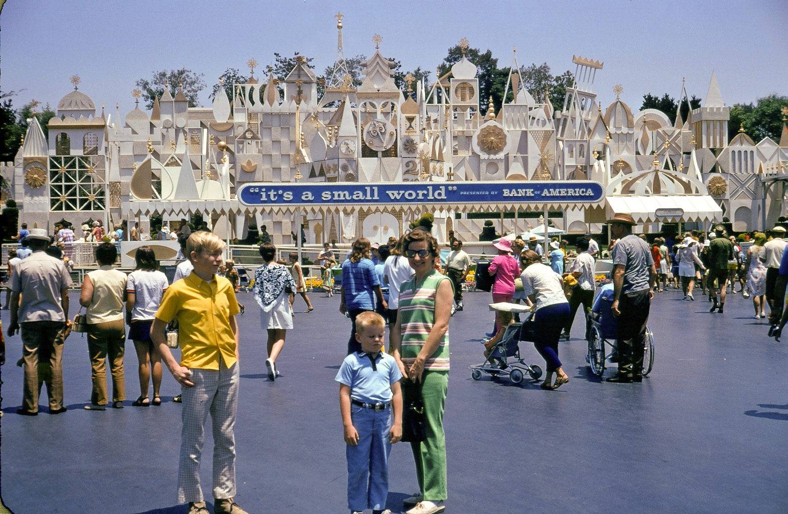 Return of the ill-tempered teen. I am actually wearing the same pants and shoes as in an earlier picture. Sometimes I'm surprised my parents didn't just dump me on some roadside back then. I wasn't a troublemaker, but I sure was a grouchy SOB! 

I like this picture for the background: Disneyland about 1968. There is a lot going on. Bank of America tried to promote some warm and fuzzy values by sponsoring the Small World ride. The effects of that, I will leave to the viewer's imagination.

My Dad took the picture, as usual. There's little brother and my Mom is still alive and kicking at age 83. View full size.