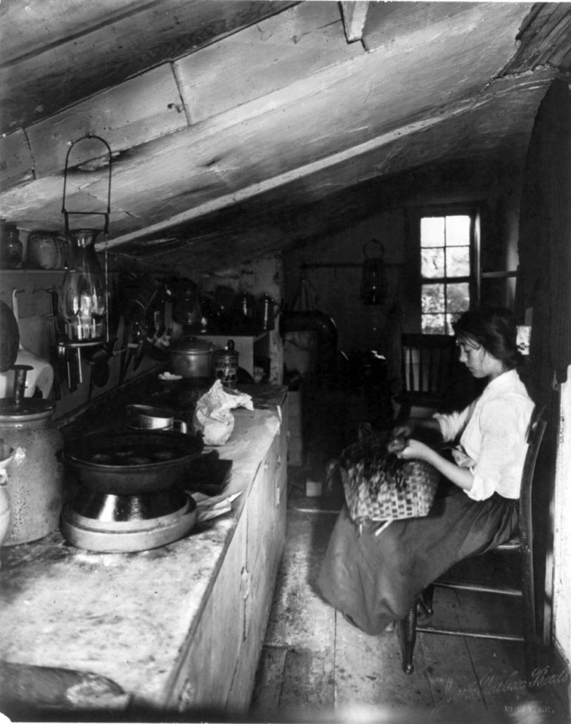 Photo of: Evelyn: c. 1909 -- Evelyn, a maid, seated in a New York kitchen with a basket on her lap. Photographed by Jessie Tarbox Beals, c. 1909. View full size.