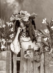 A glamour photograph of a girl posing with flowers. Photograph by J. Maurer, c. 1902. View full size.
