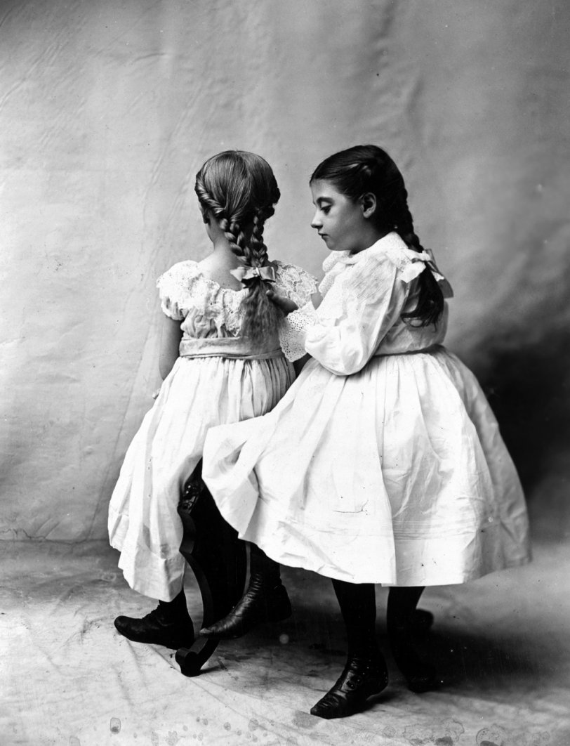 Photo of: Young Models: c. 1900 -- A portrait of two girls seated, one looking at the braided hair of the other. The photograph is by the Tonnesen Sisters of Chicago, c. 1900. The Tonnesen Sisters ran one of the country's first photo studios for the purpose of creating advertising images. They also ran one of the first professional modeling agencies. View full size.